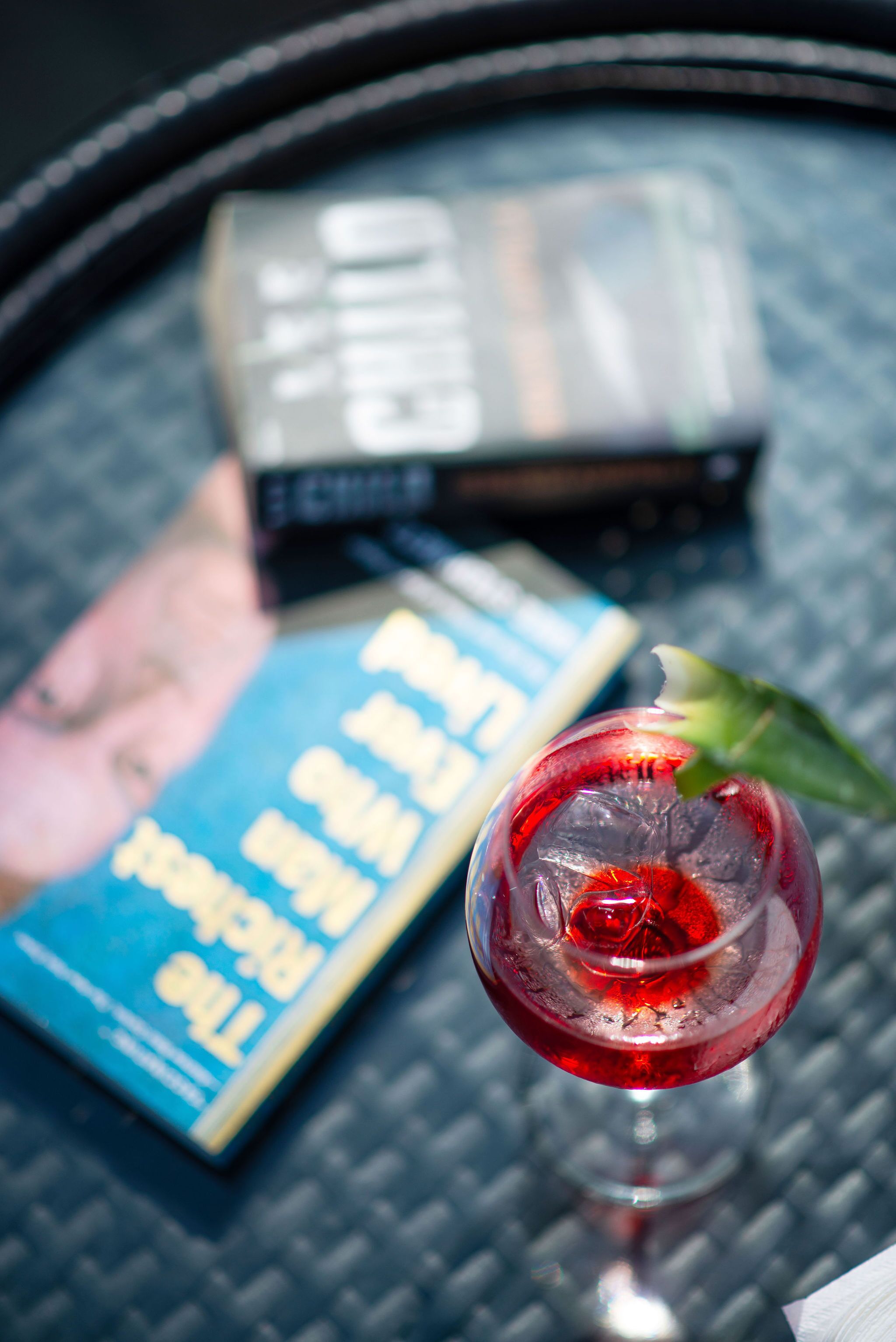 A cocktail glass with a red drink and a leaf garnish on a table with a book and a box.