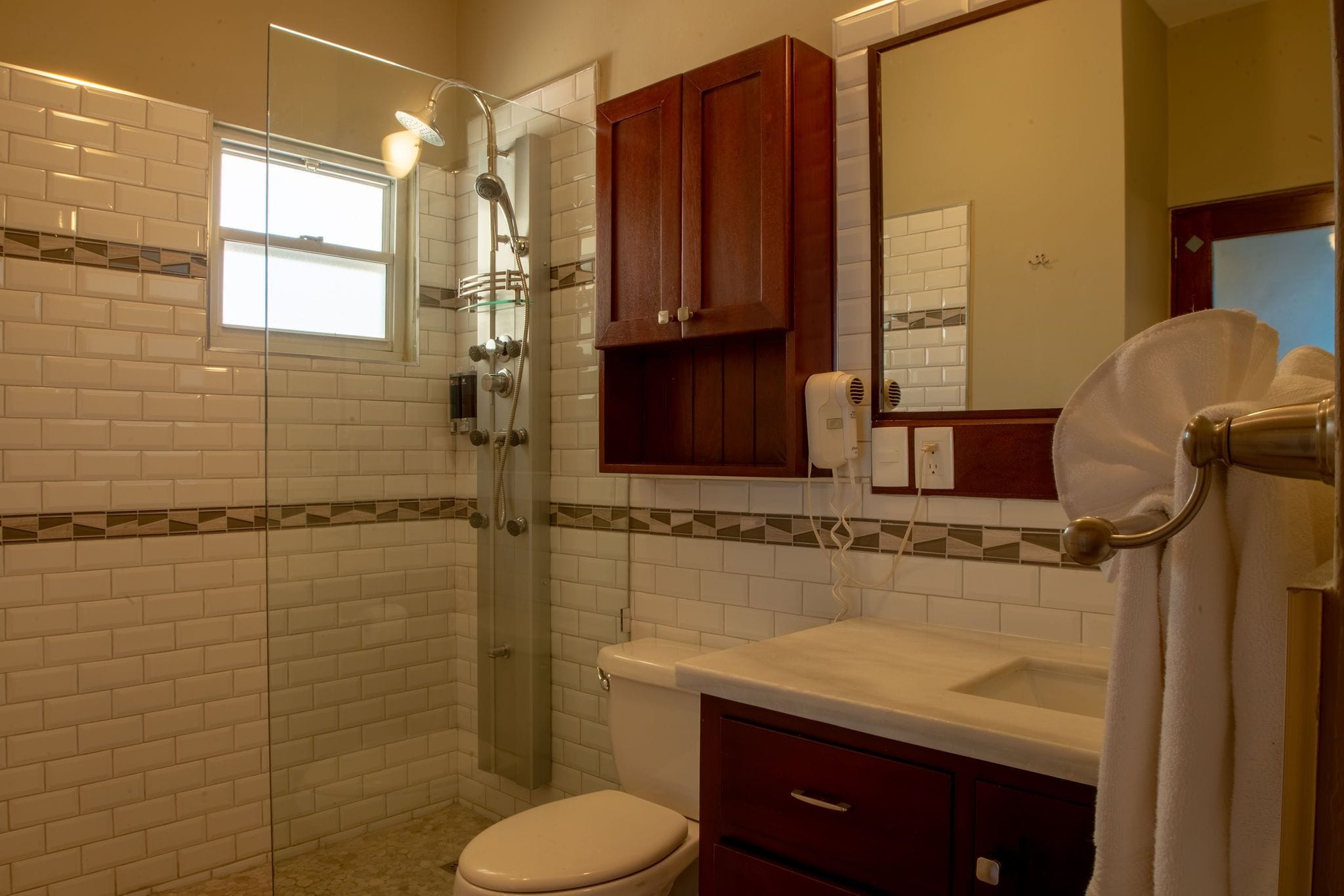 A bathroom with white subway tiles, a glass-enclosed shower, a wooden cabinet, a white sink, and a towel rack.