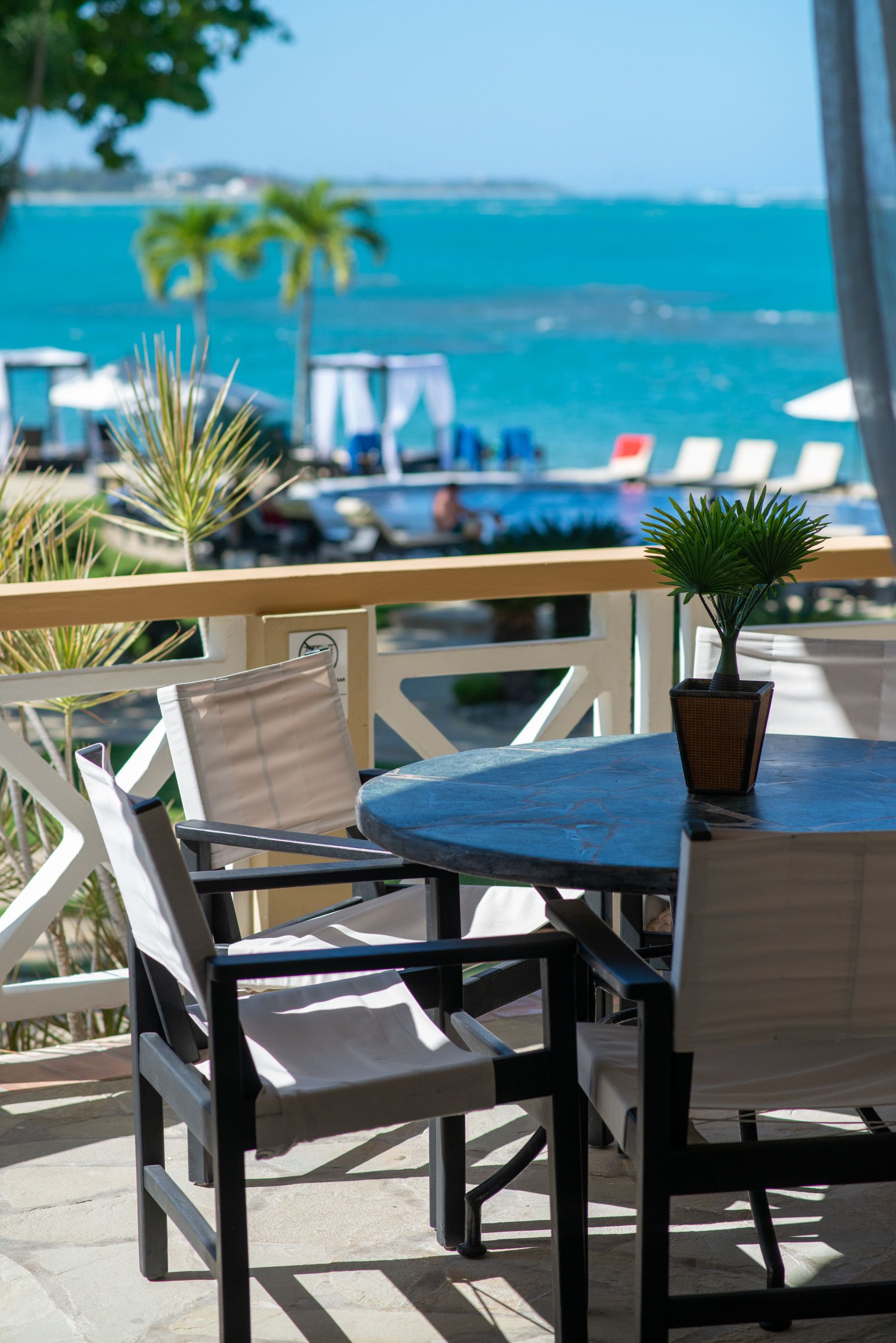 Un patio con una mesa y sillas, una planta en maceta y vistas al océano y sombrillas de playa.