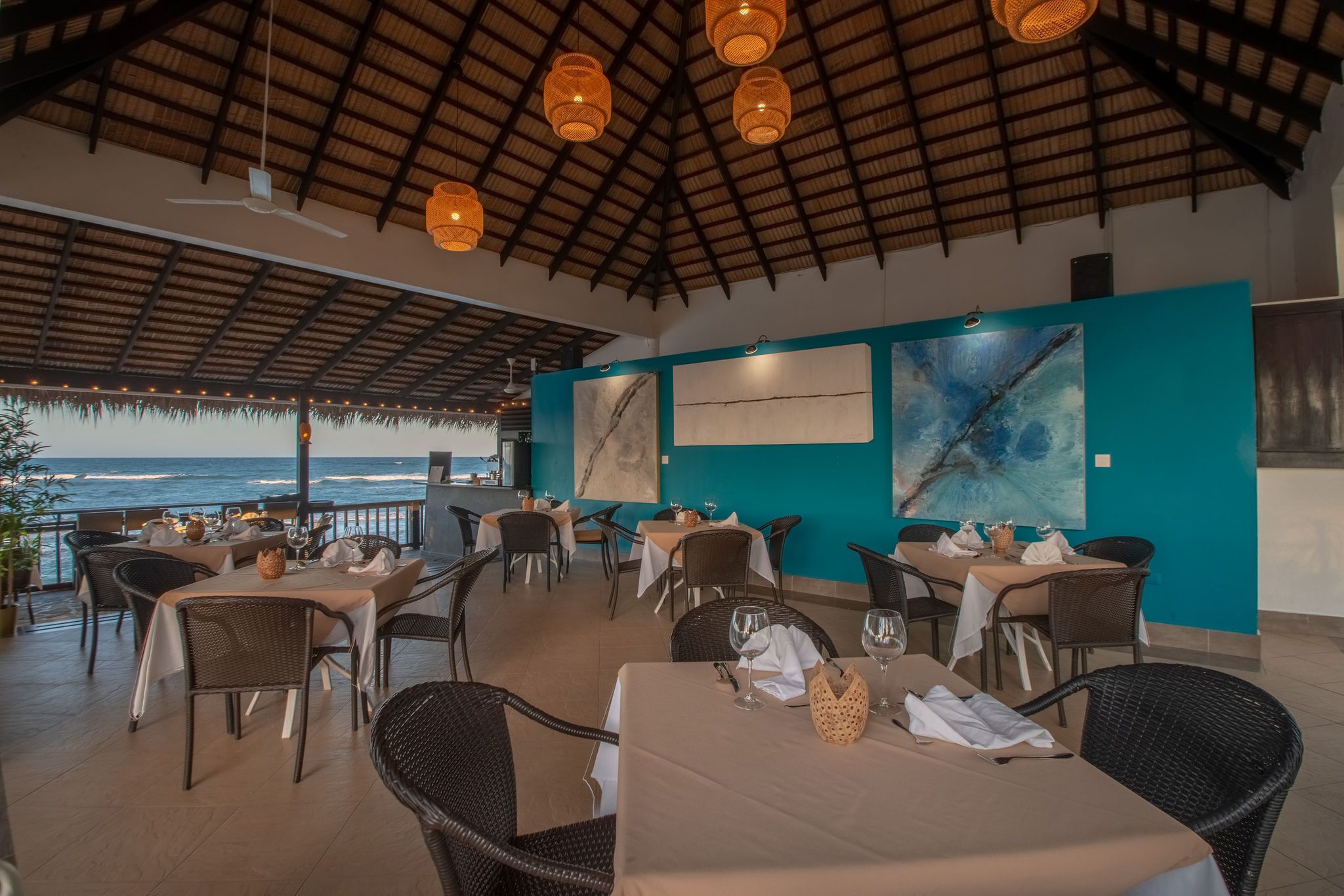 Area esterna con zona pranzo, tavoli e sedie, vista sull'oceano e opere d'arte alle pareti.