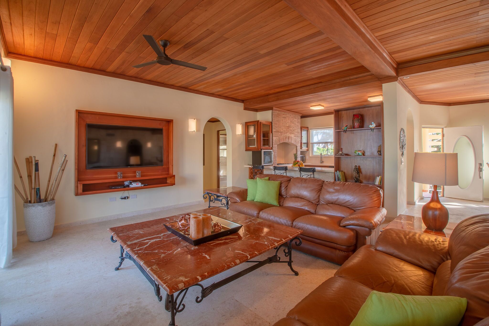A spacious living room with a leather sofa, a marble coffee table, and a television mounted on the wall.
