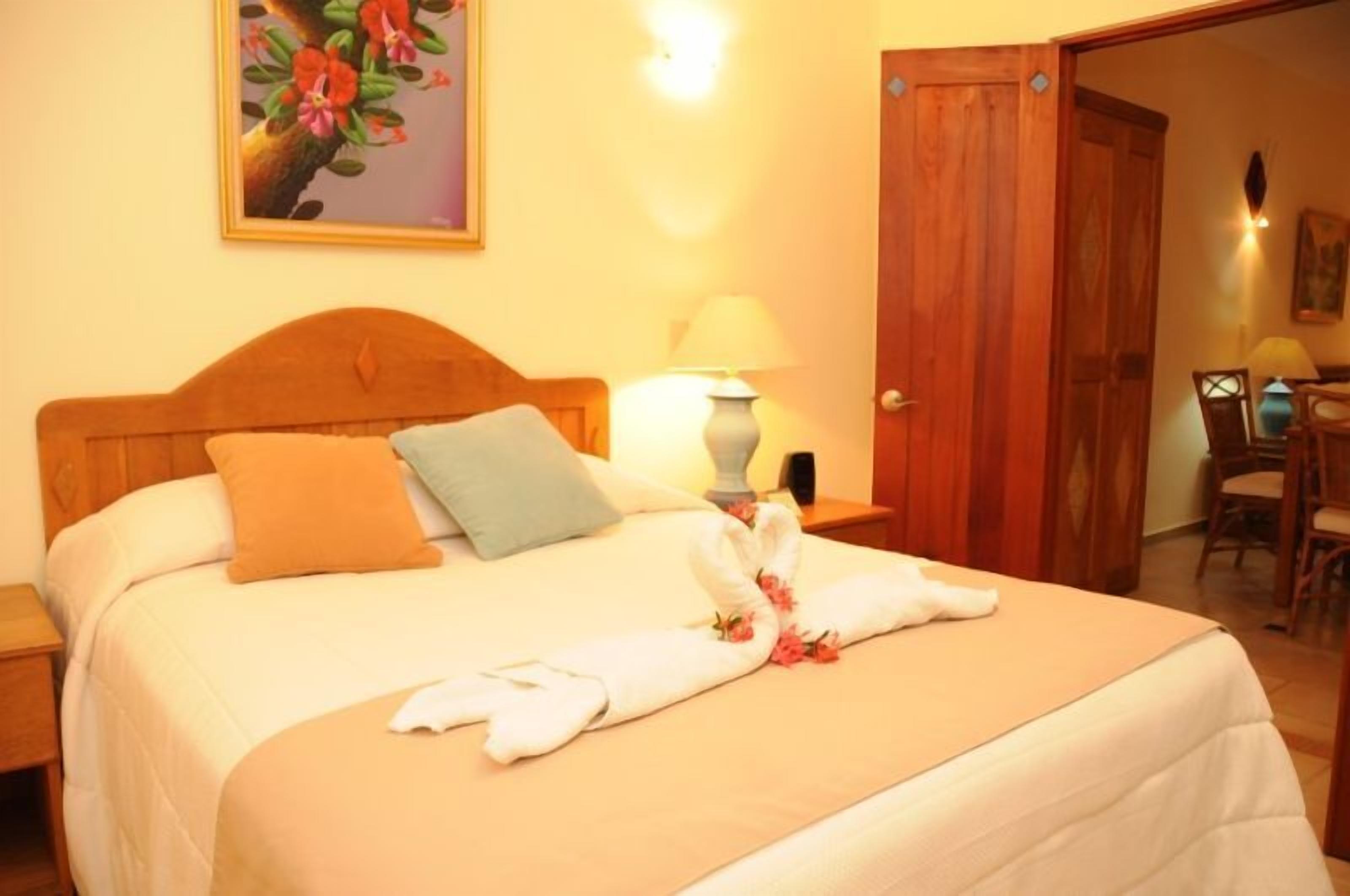Una cama bien hecha con almohadas, una lámpara de noche y una toalla con motivos florales en una habitación de hotel.