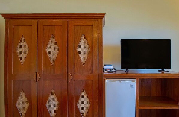 Un mueble de madera con cortes en forma de diamante, un televisor de pantalla plana y un refrigerador pequeño.