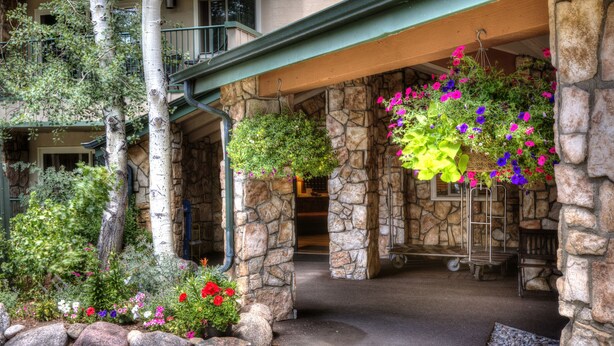 A stone building with a covered entrance, a stone bench, and hanging flower baskets. - Falcon Point (Avon)