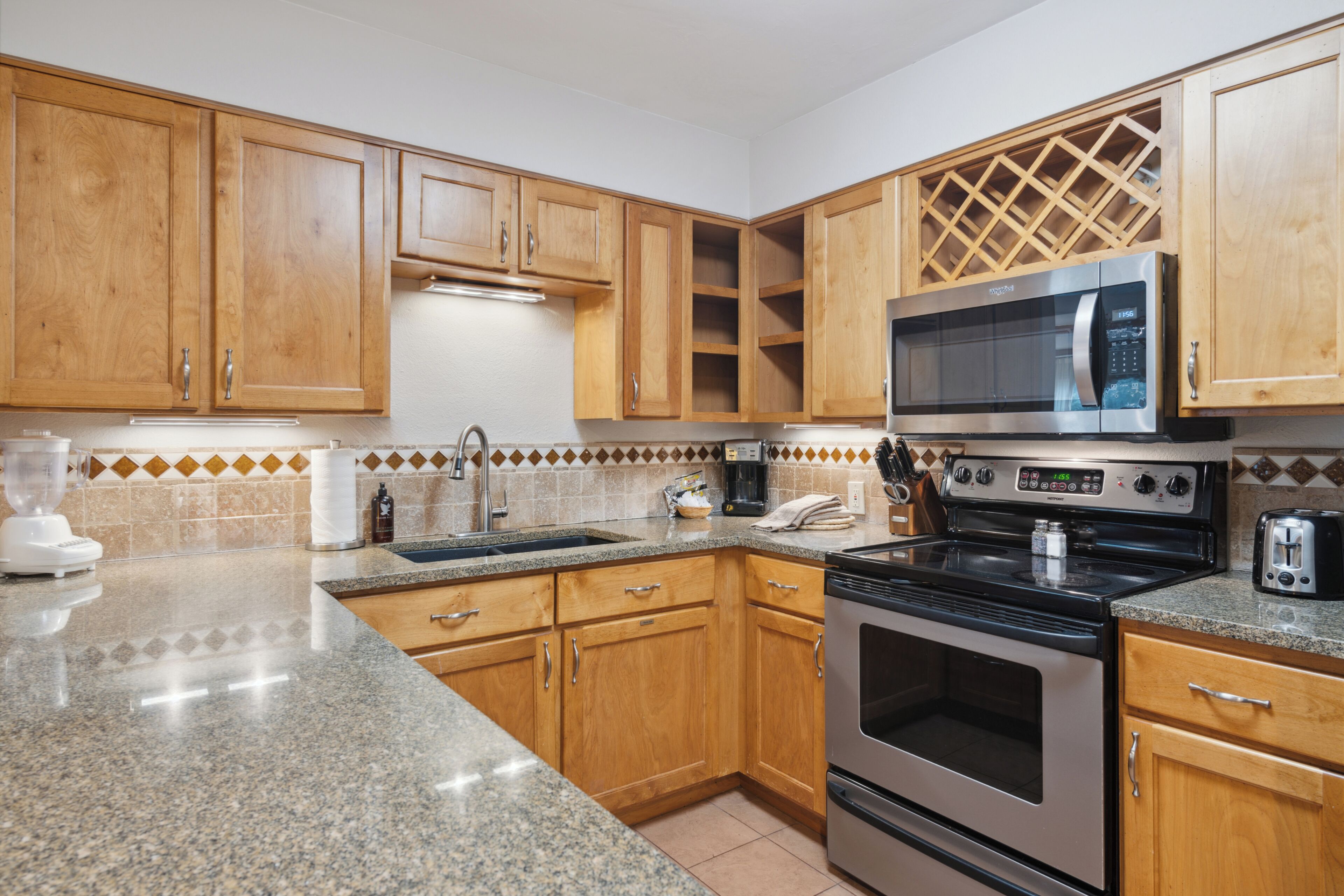 A kitchen with wooden cabinets, a granite countertop, a stainless steel stove, a microwave, and a toaster.