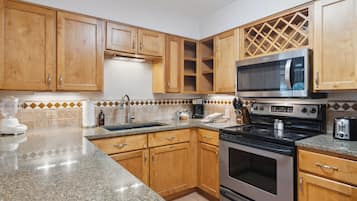 A kitchen with wooden cabinets, a granite countertop, a stainless steel stove, a microwave, and a toaster.
