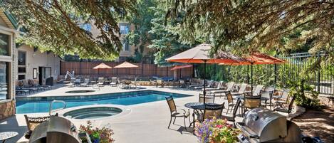 A poolside area with a hot tub, lounge chairs, and barbecue grills.