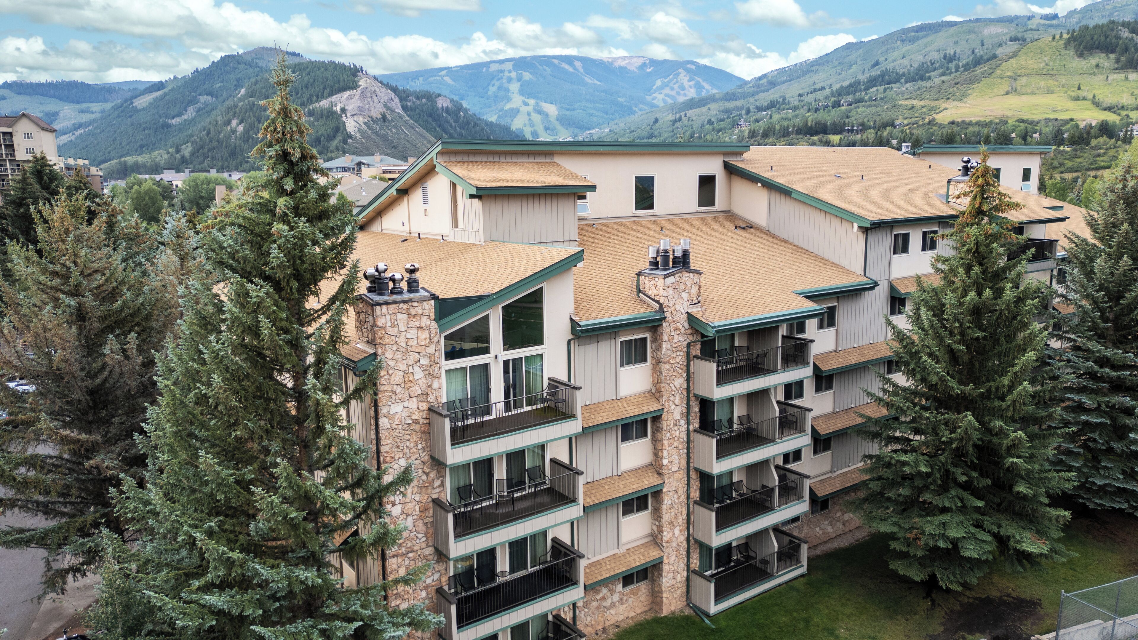 A multi-story hotel with a stone facade, balconies, and a view of mountains.