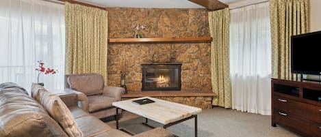 A living room with a stone fireplace, leather sofa, and a television on a wooden stand.