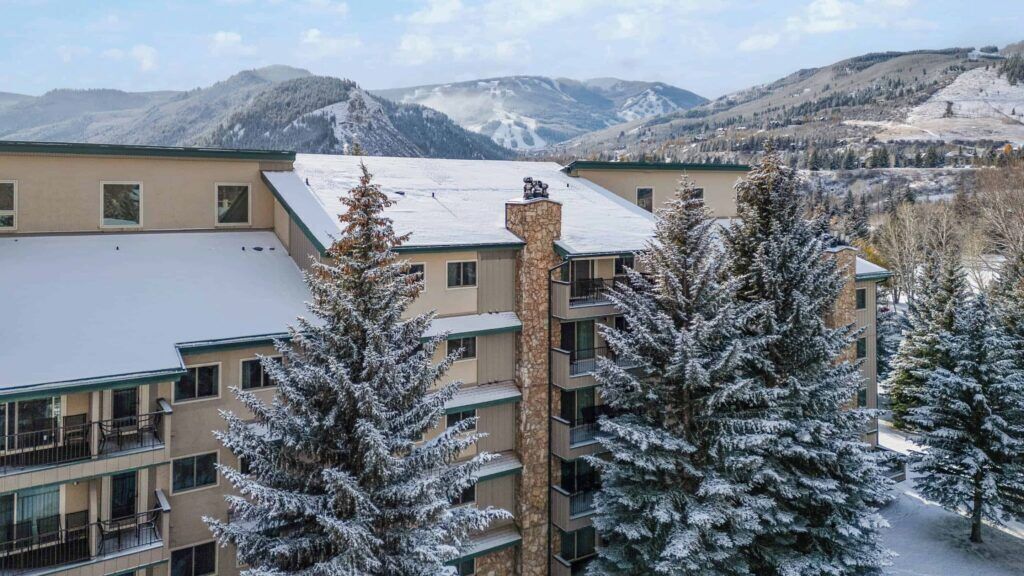 A multi-story building with balconies, surrounded by snow-covered trees and mountains in the background.