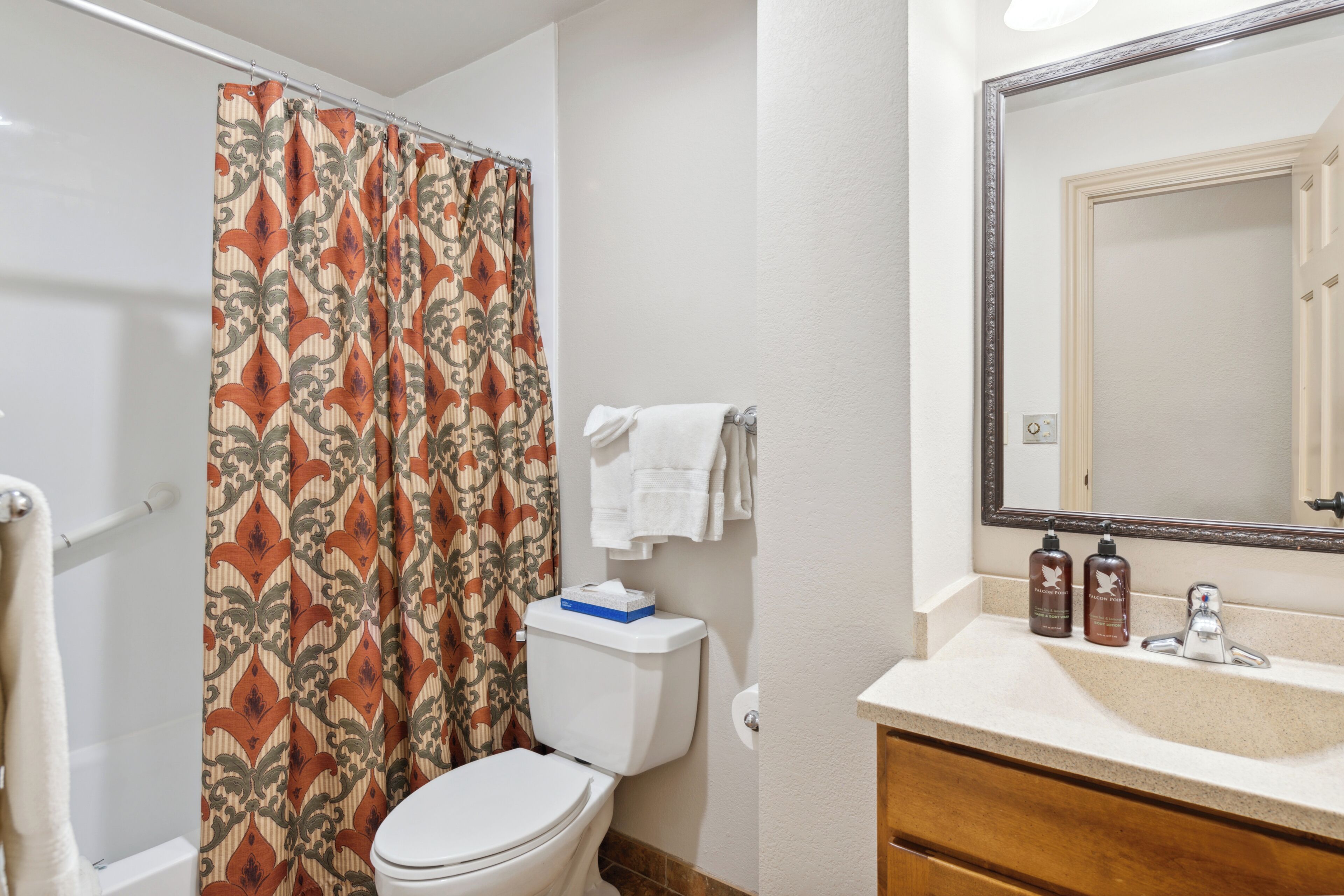 A bathroom with a toilet, shower curtain, sink, and mirror.