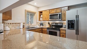 A modern kitchen with granite countertops, stainless steel appliances, wooden cabinets, and a window with a view of trees. - Falcon Point (Avon)