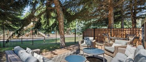 An outdoor patio area with wicker furniture, including sofas and tables, surrounded by trees.