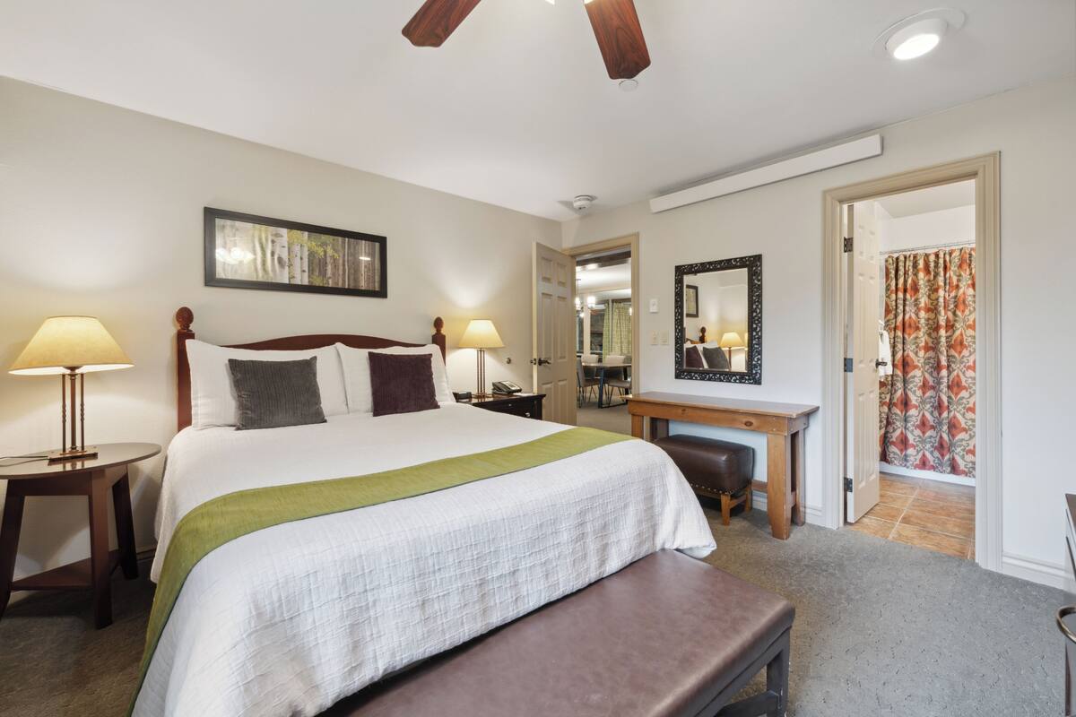 A hotel room with a bed, bedside tables, a desk, and a mirror.