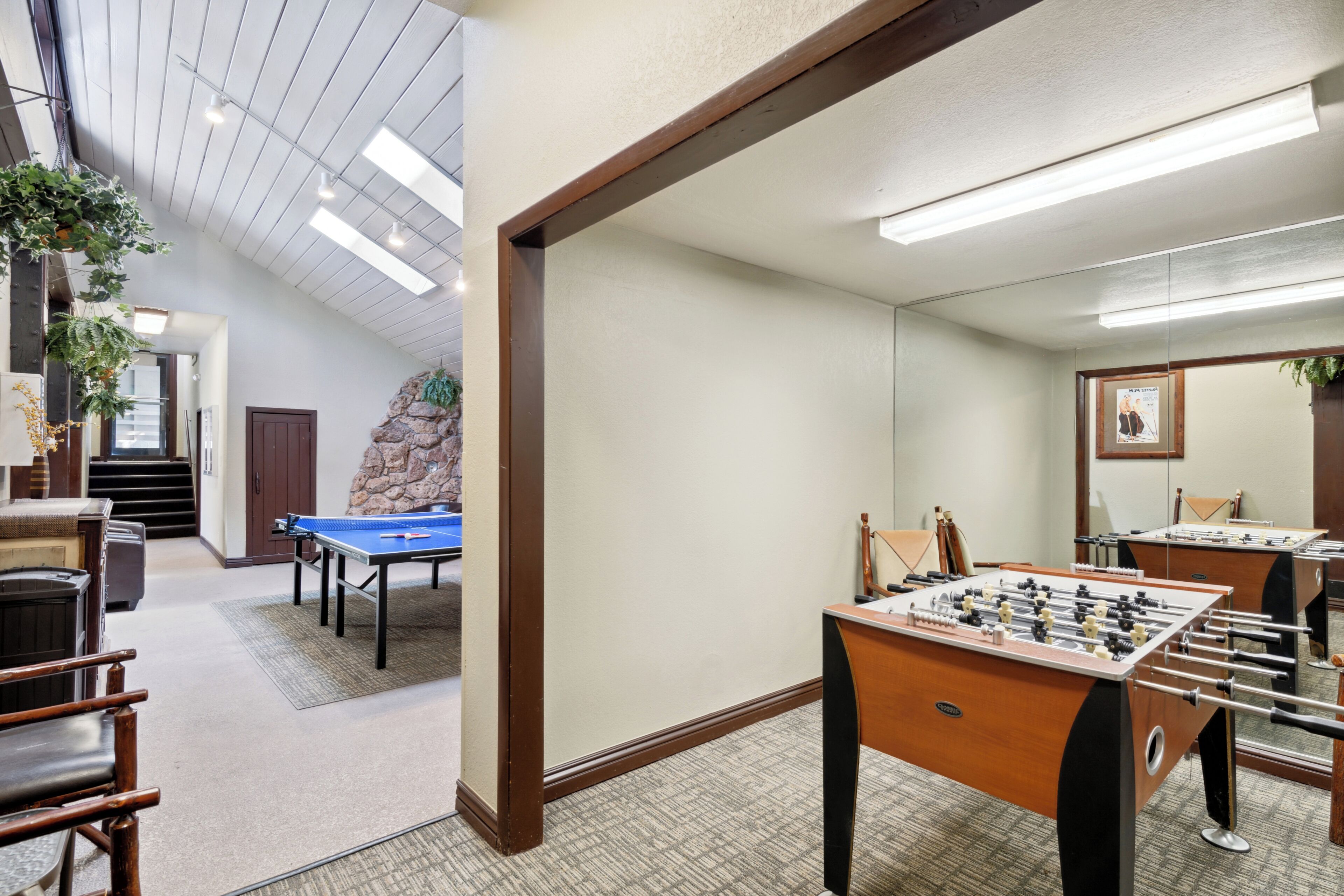 A room with a pool table, a foosball table, and a large mirror.