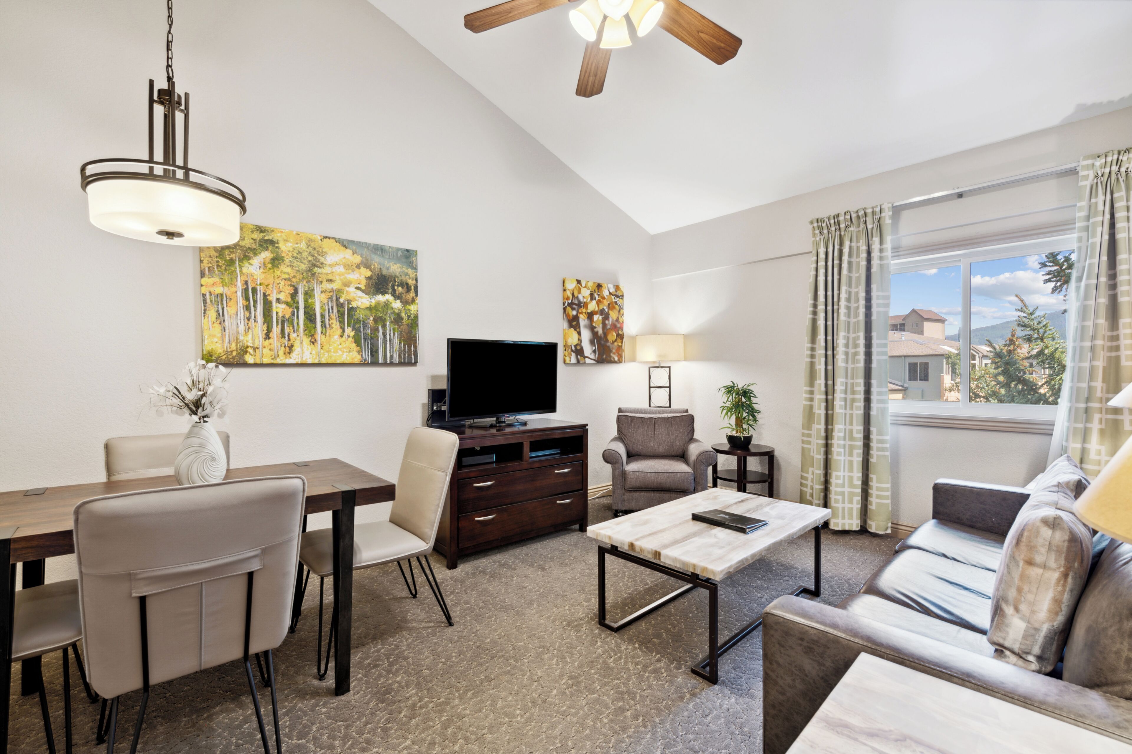 A modern living room with a dining area, a flat-screen TV, a sofa, and a ceiling fan.