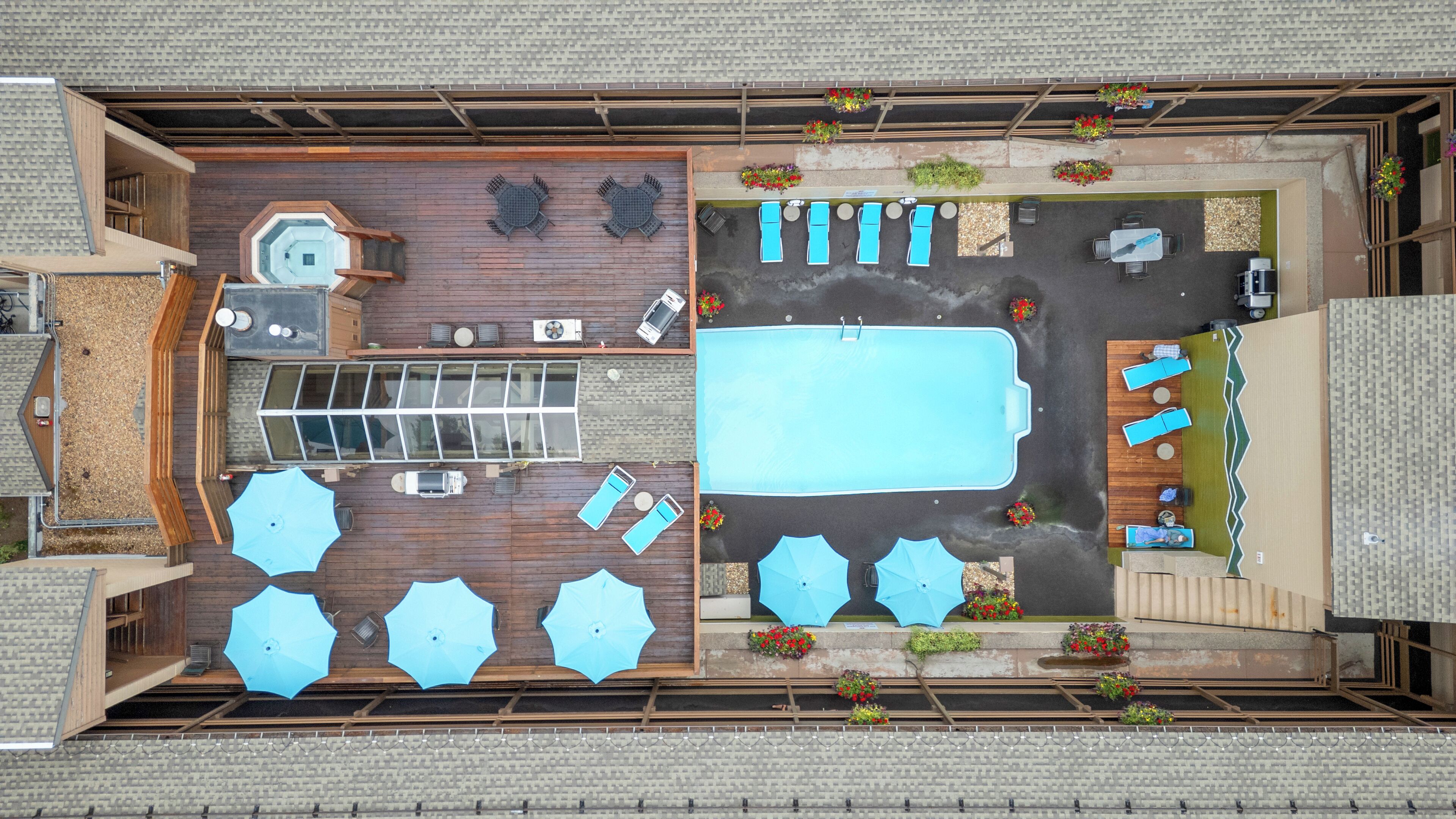 An aerial view of a rooftop pool area with a swimming pool, sun loungers, umbrellas, and a seating area with tables and chairs.