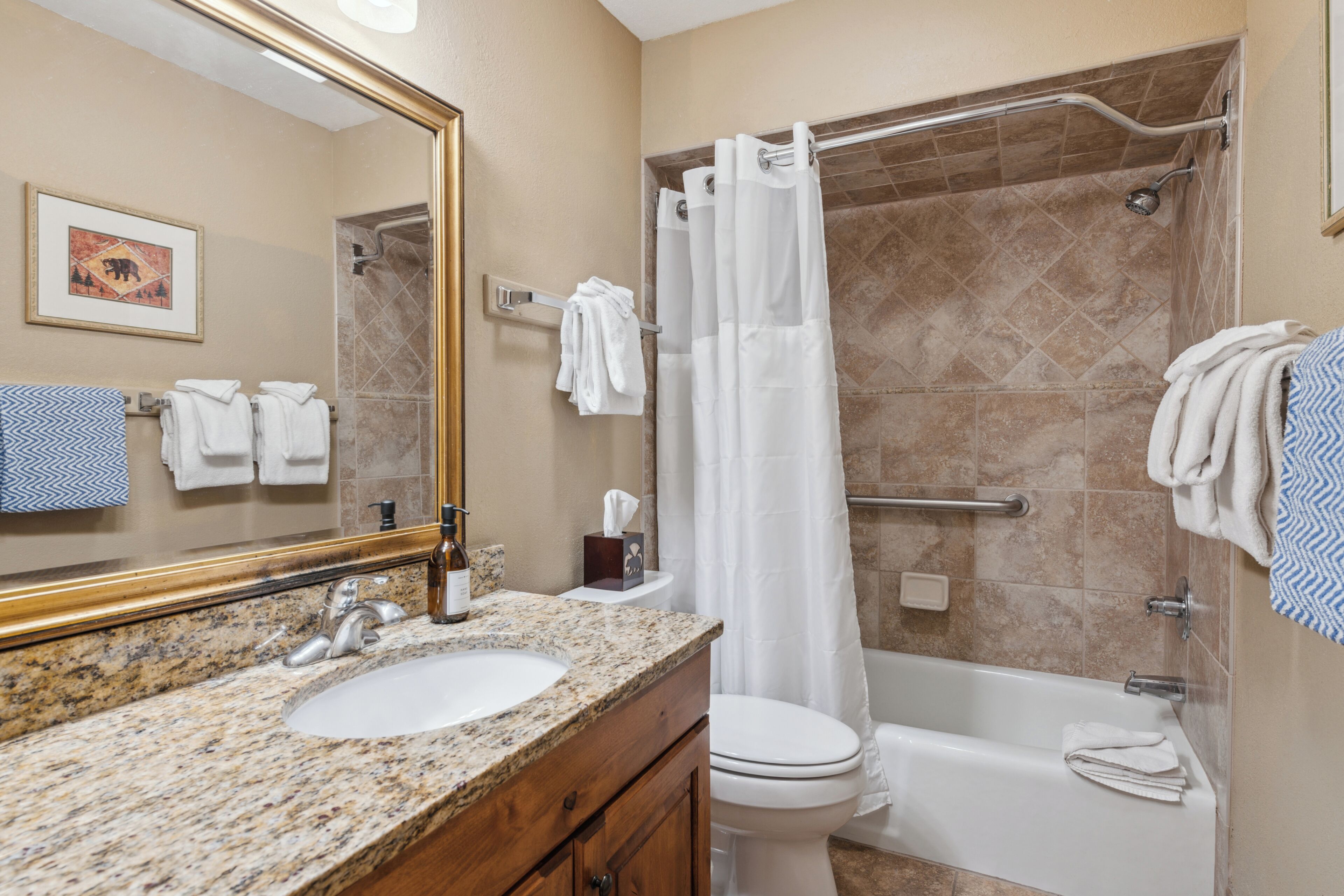A bathroom with a granite countertop sink, a white toilet, a bathtub, and a shower with a glass door.
