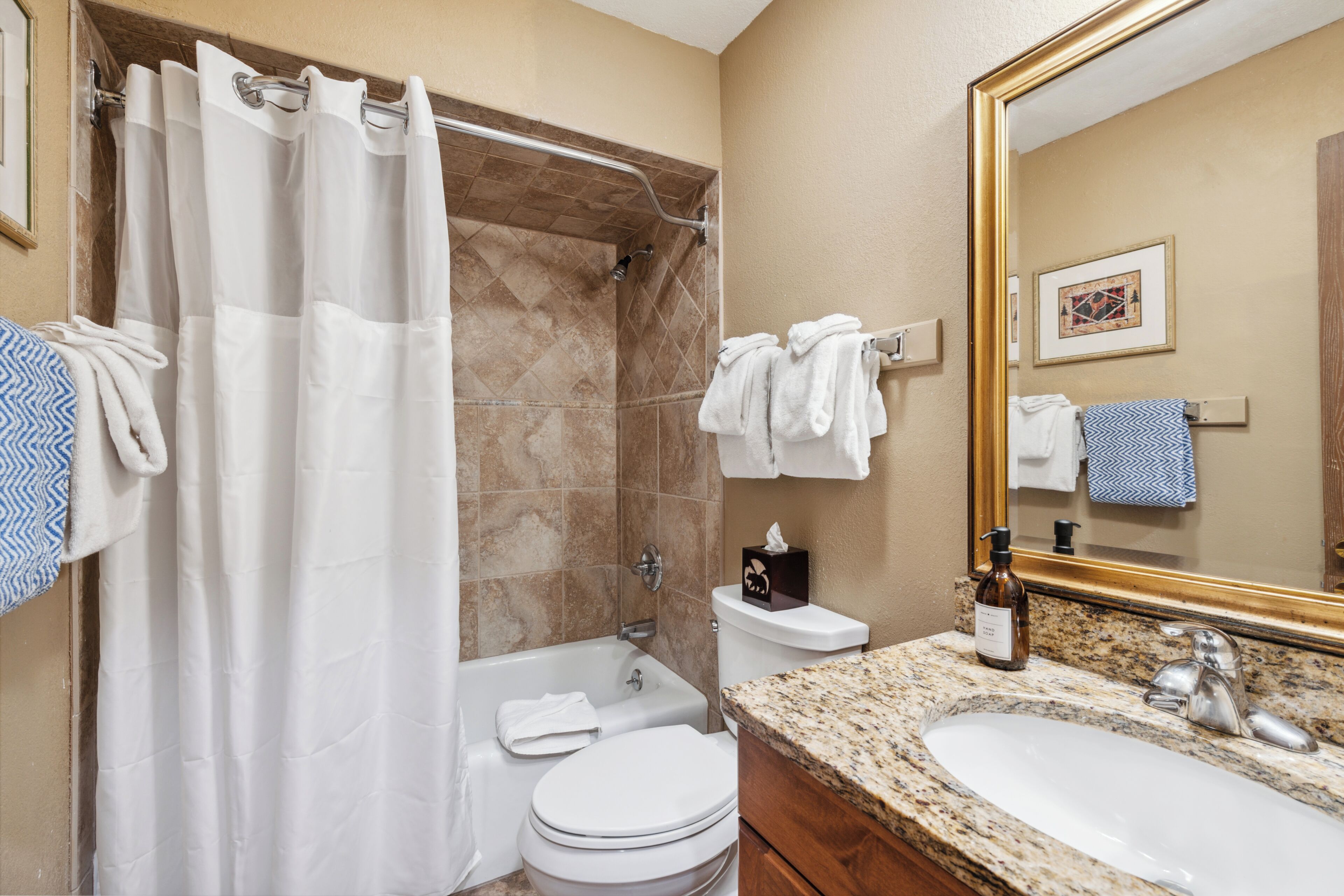 A bathroom with a shower, toilet, sink, and a large mirror.