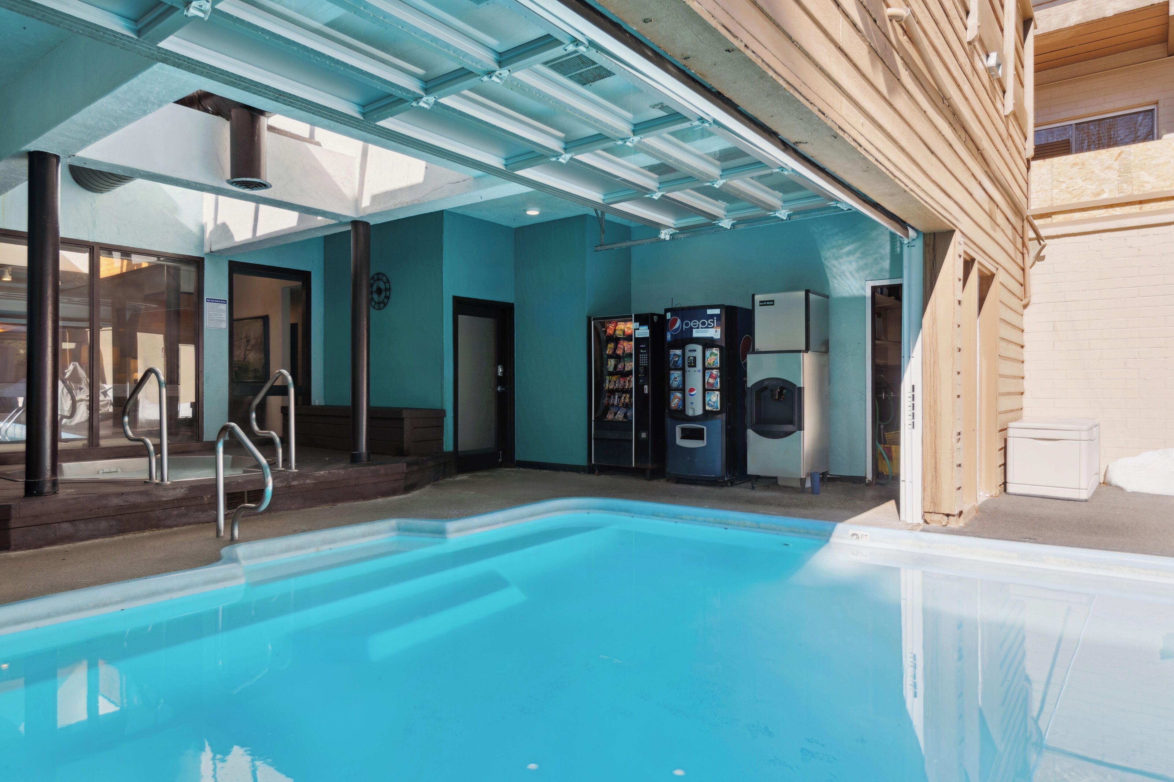 Ein überdachter Swimmingpool mit großen Glaswänden, ein Getränkeautomat und ein Warmwasserbereiter.