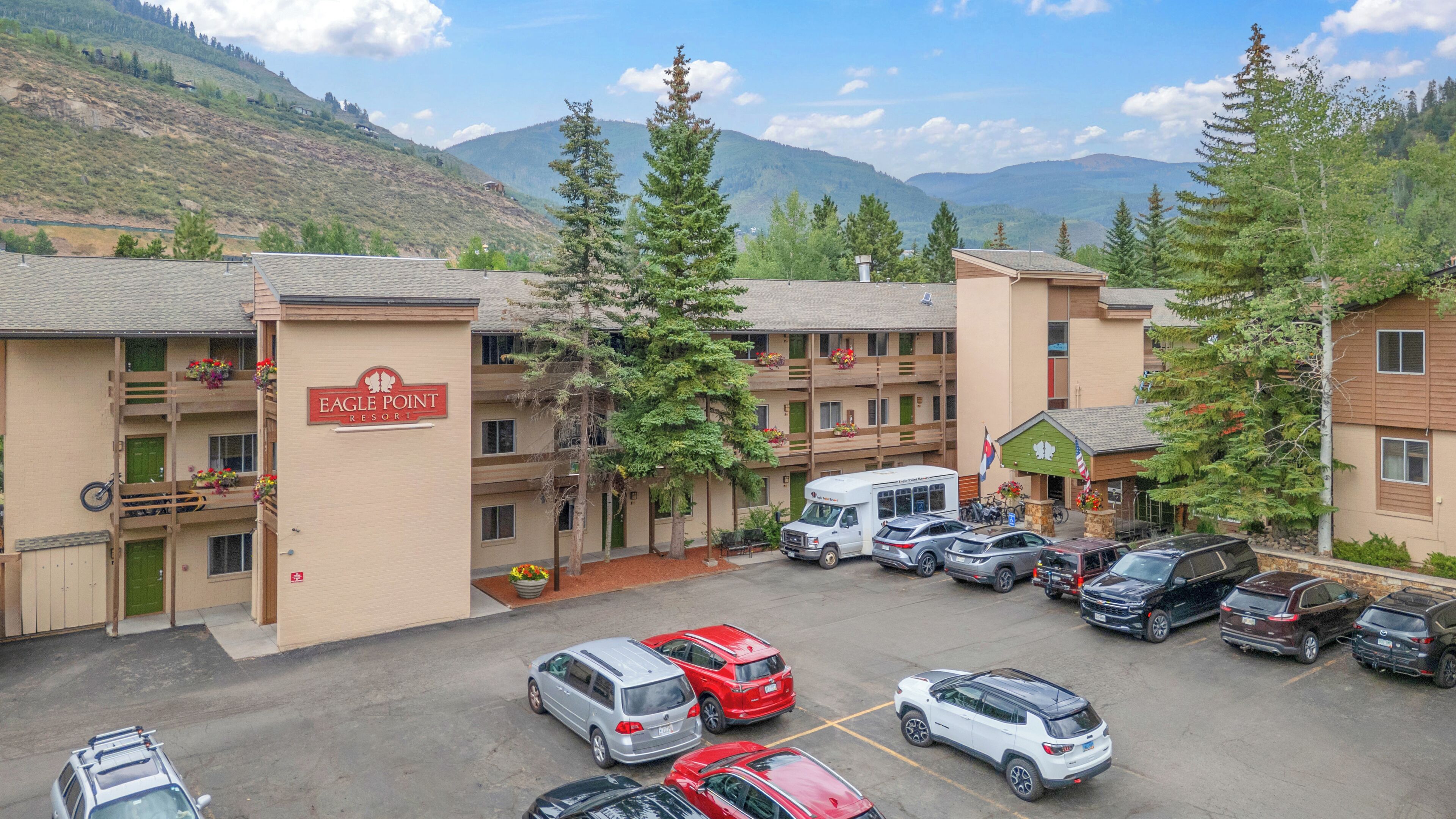 Un estacionamiento con varios autos, una camioneta blanca y un edificio con la leyenda 'Eagle Point Resort'.