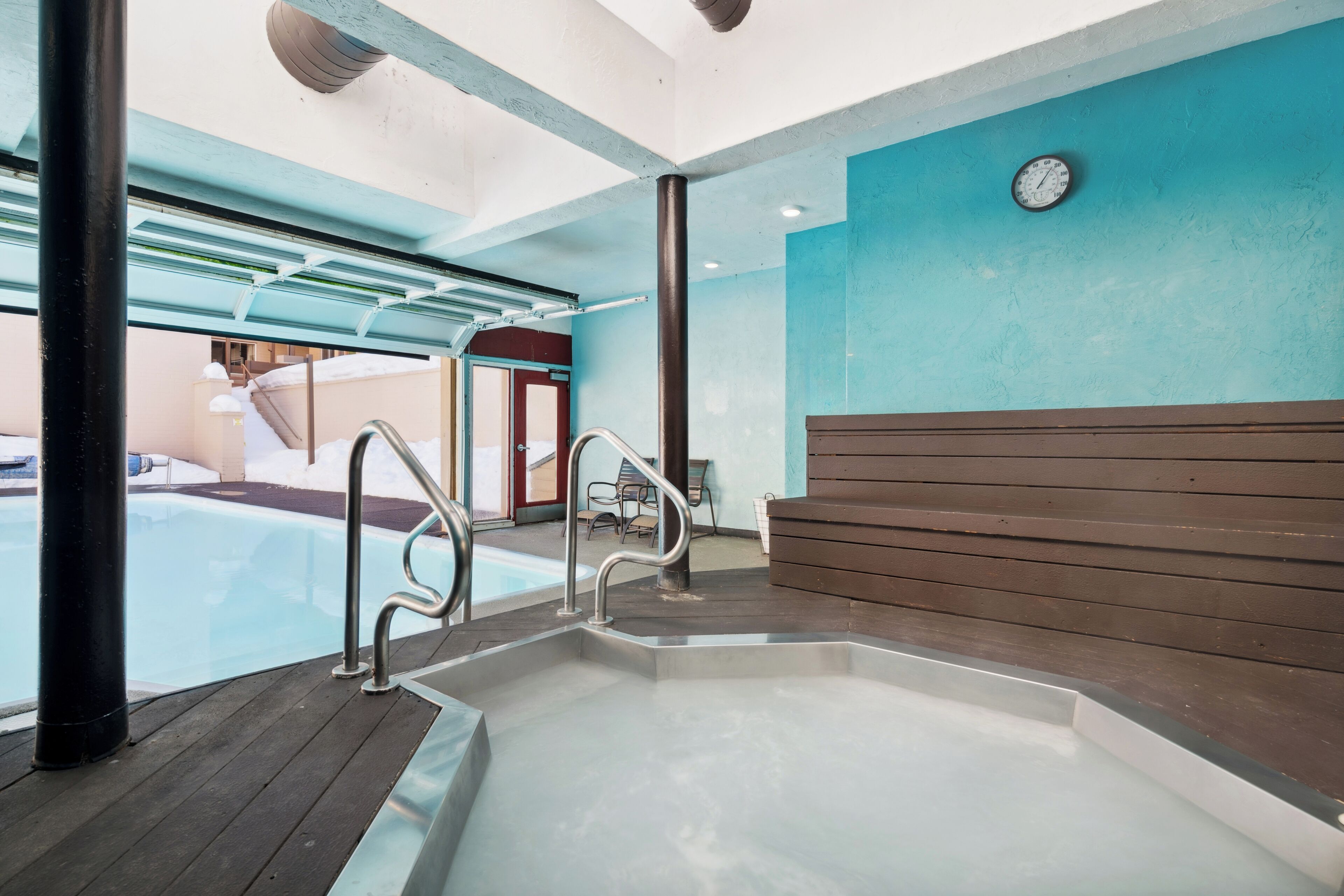 Ein Whirlpoolbereich mit einer Holzbank, Metallgeländern und Blick auf einen Pool.