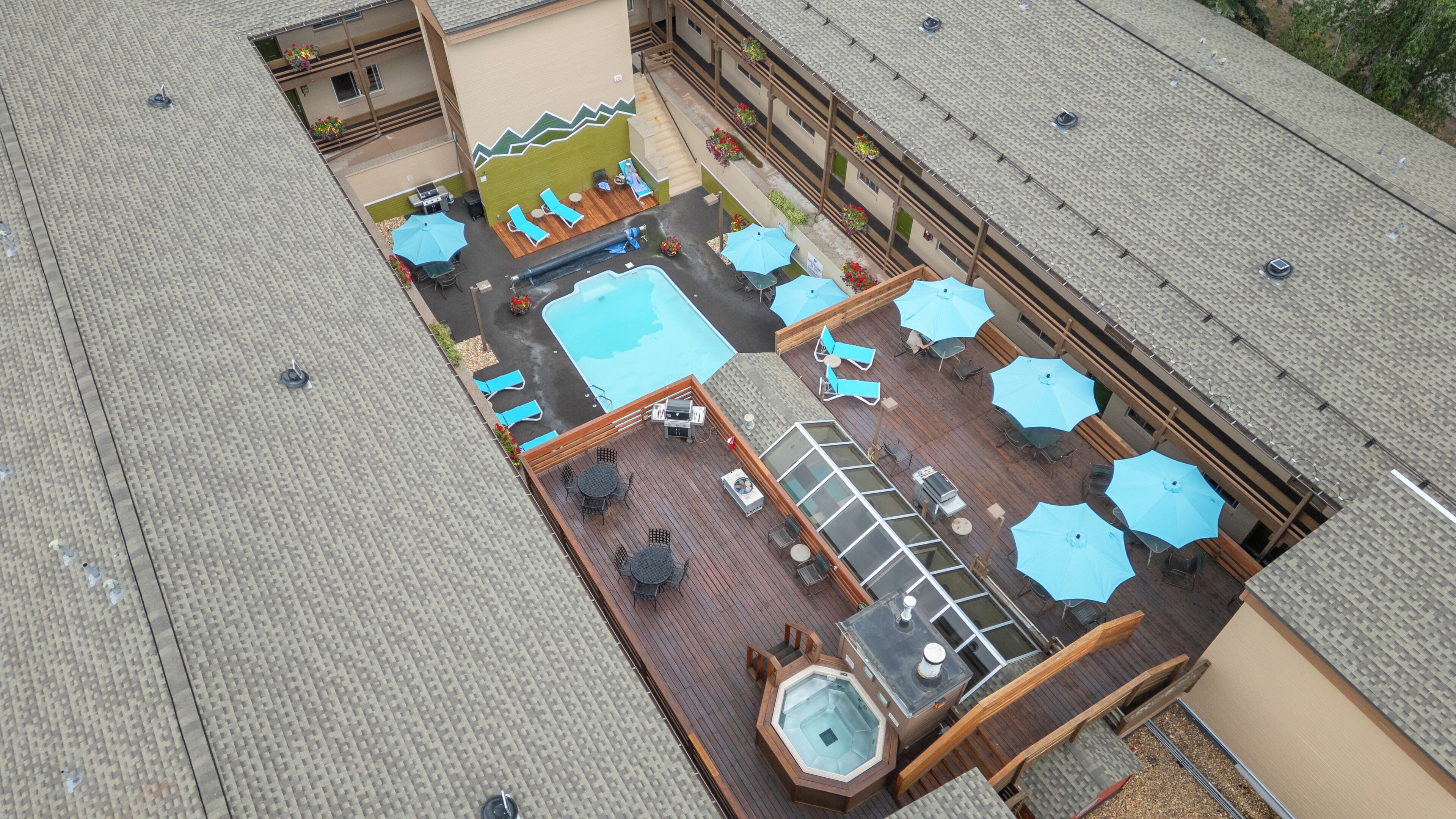 Vue aérienne d’un toit-terrasse aménagé avec une piscine, des chaises longues, des parasols et un jacuzzi.