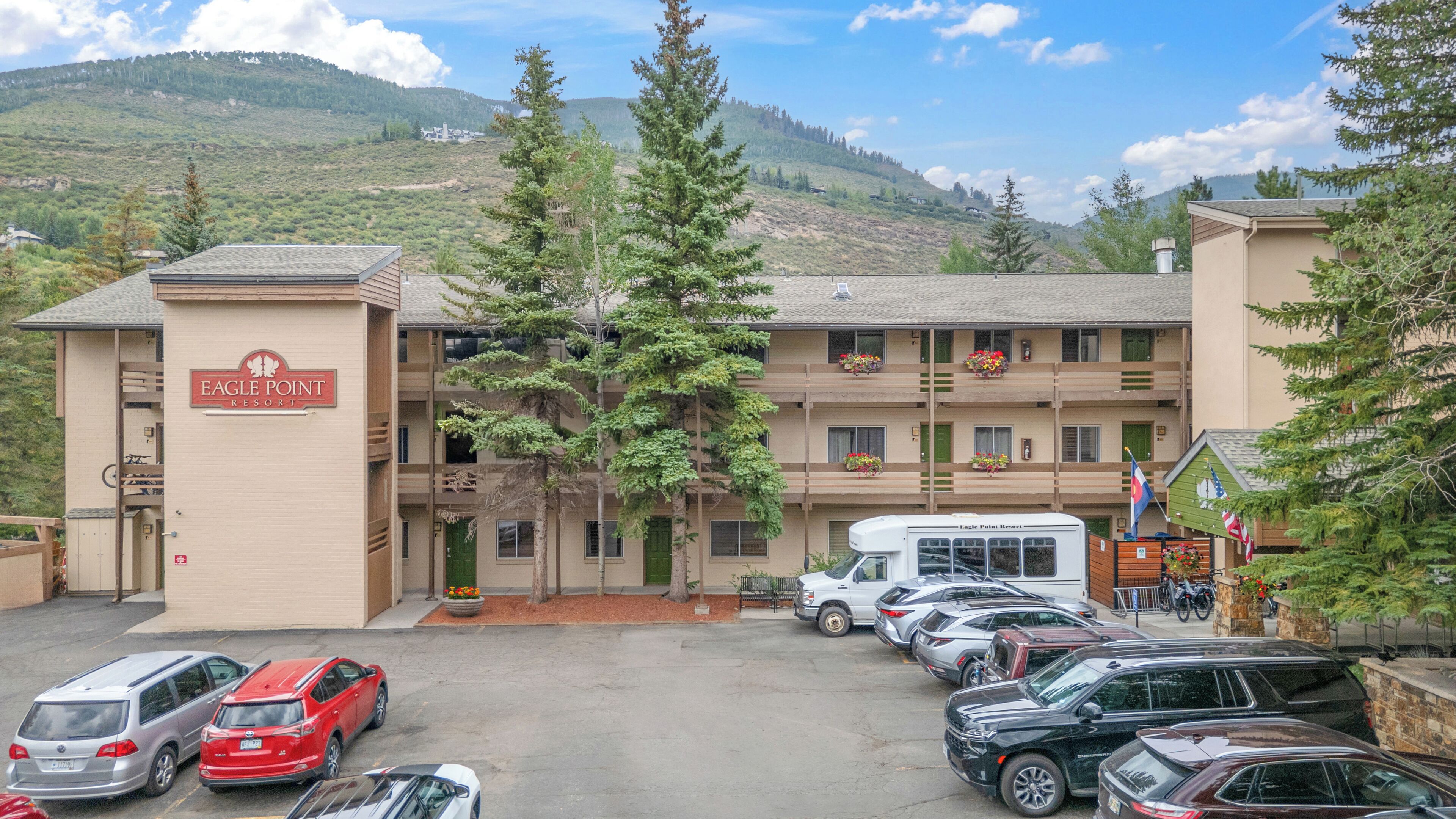 Un immeuble à plusieurs étages, sur lequel on peut lire l’inscription « Eagle Point Resort ». Plusieurs voitures sont garées devant, et l’immeuble possède un balcon orné de plantes en pot.