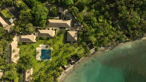 An aerial view of a coastal property with multiple houses, a swimming pool, and a beach. - Alila Manggis, Bali (Manggis)