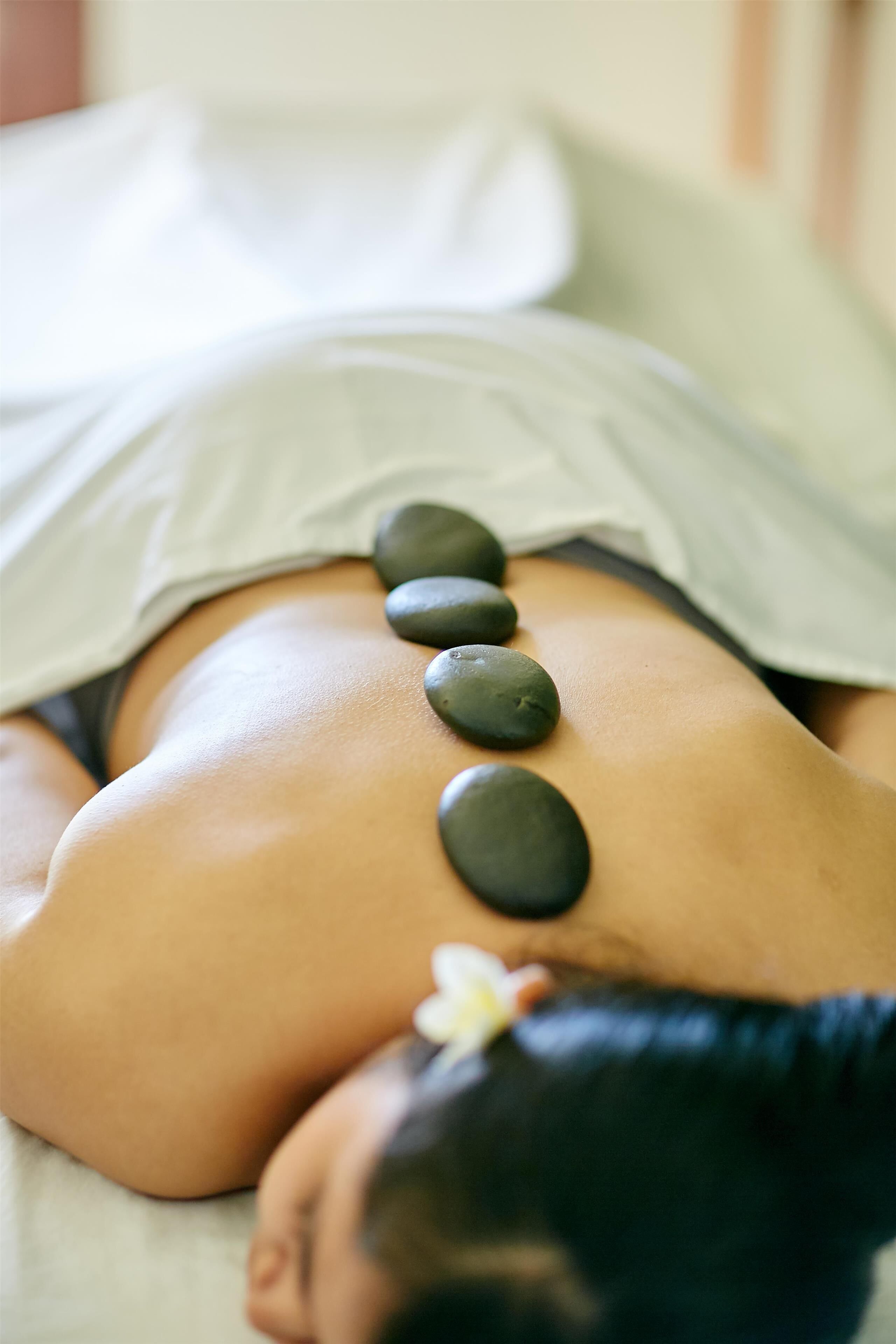 A person receiving a back massage with stones placed along their spine.