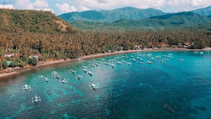 An aerial view of a coastal area with clear turquoise waters, numerous boats, and a backdrop of lush green hills. - Alila Manggis, Bali (Manggis)