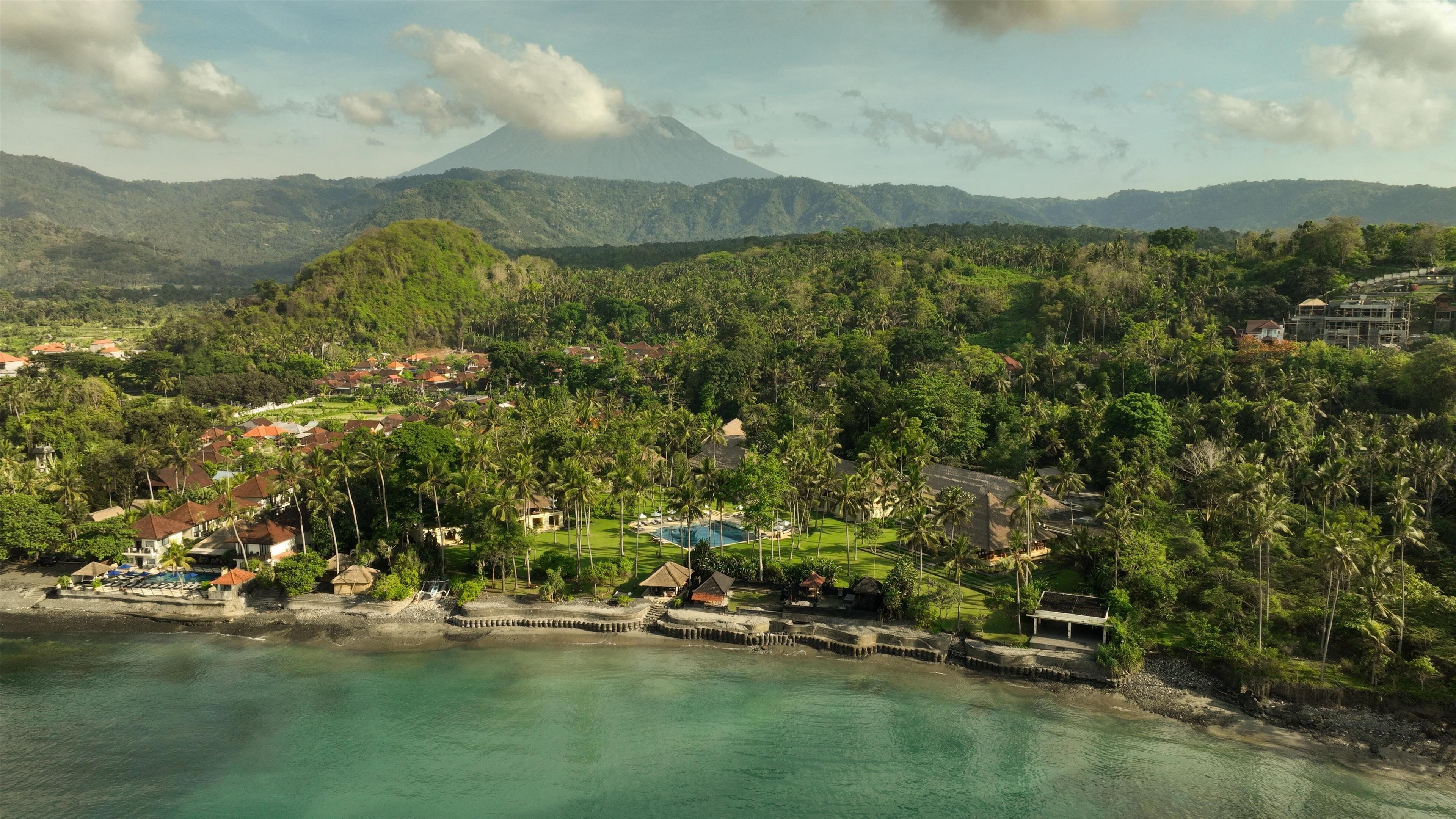 A coastal resort with a swimming pool, beachfront villas, and a view of a volcano in the background.