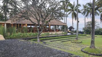 Un resort con un edificio de techo de paja, palmeras y una fuente de agua.