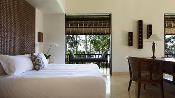 A hotel room with a bed, a desk, and a chair. There is a view of trees and a balcony outside the window.