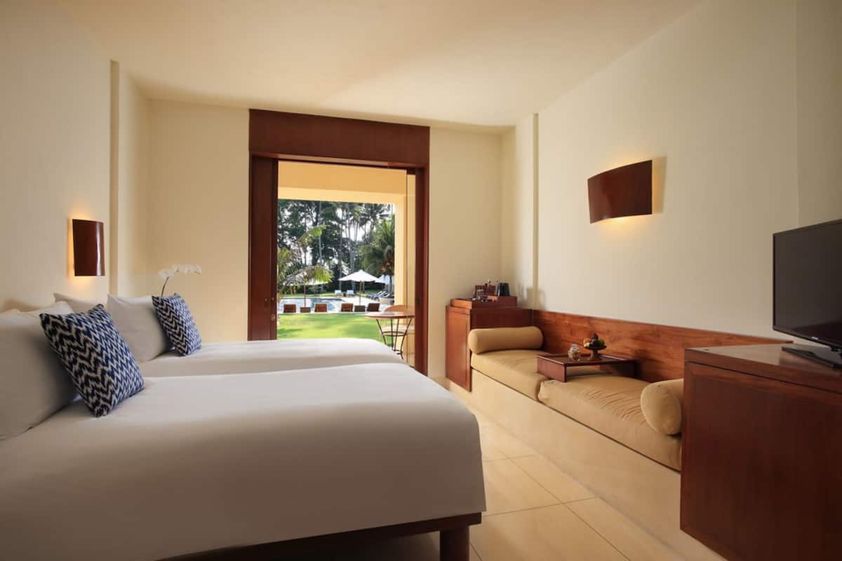 A hotel room with a large bed, a sofa, a TV, and a view of a pool and greenery.