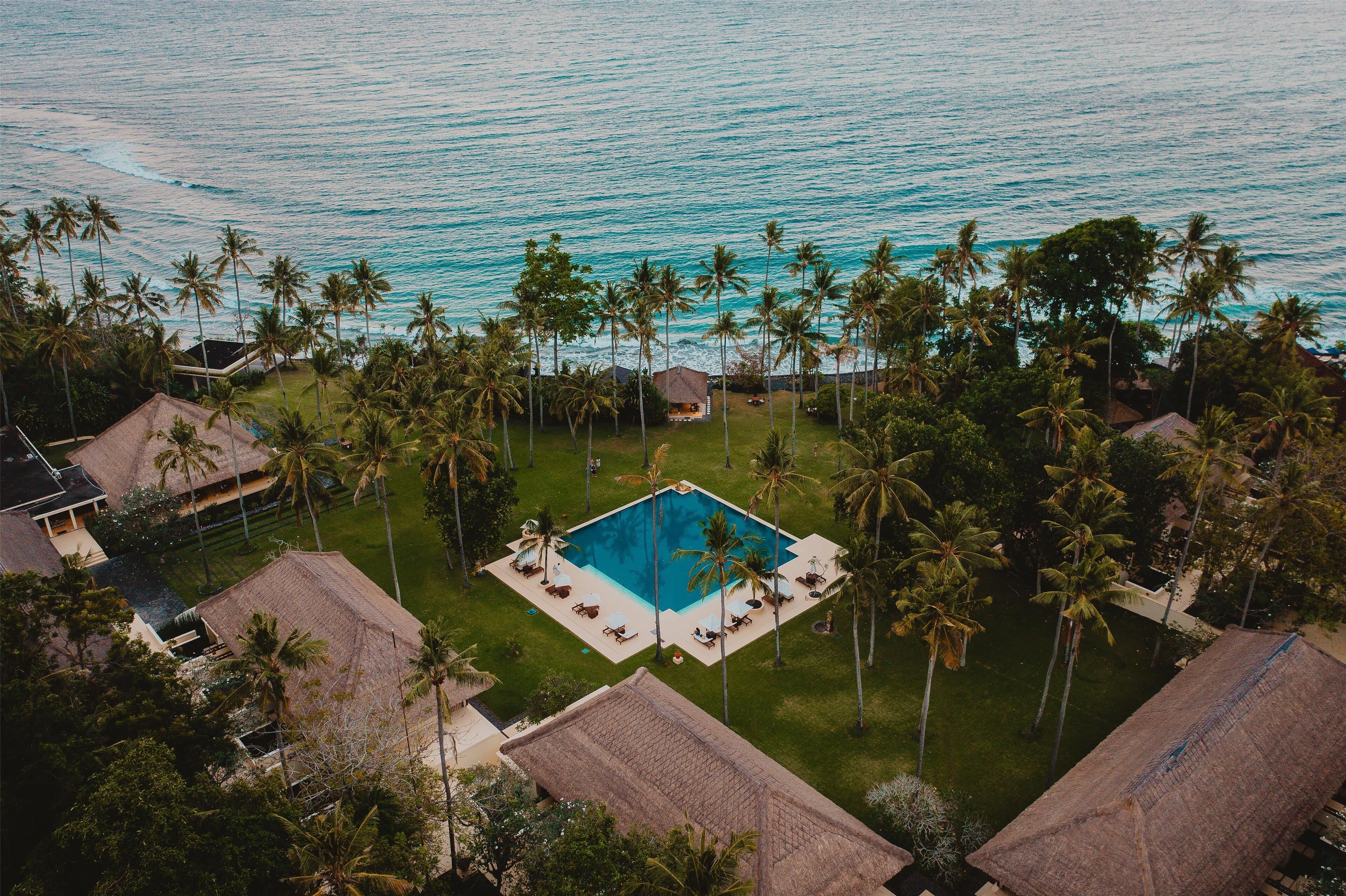 Vista aérea de un resort con una piscina central rodeada de palmeras y edificios con techo de paja.