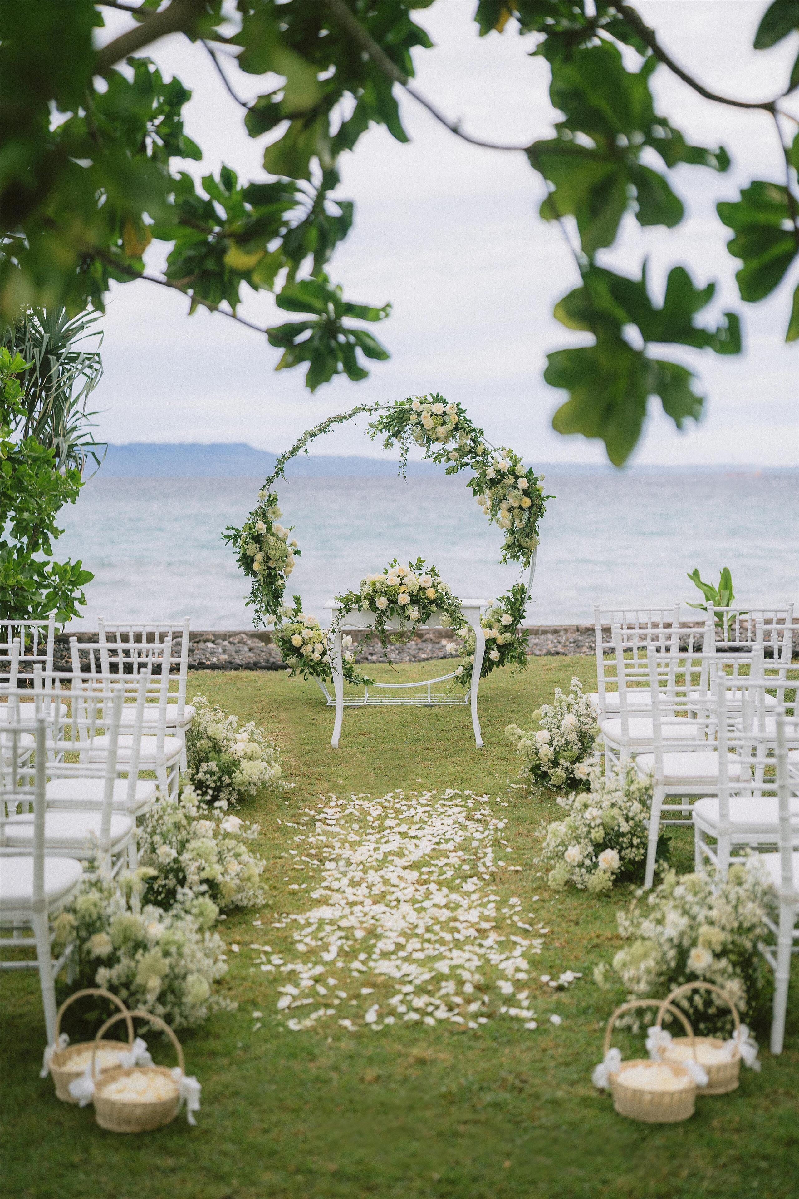 Un lugar para bodas al aire libre con sillas blancas y un arco floral.