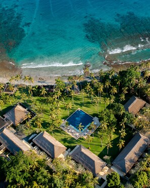 Luchtbeeld van een resort met een zwembad, palmbomen en een strand.