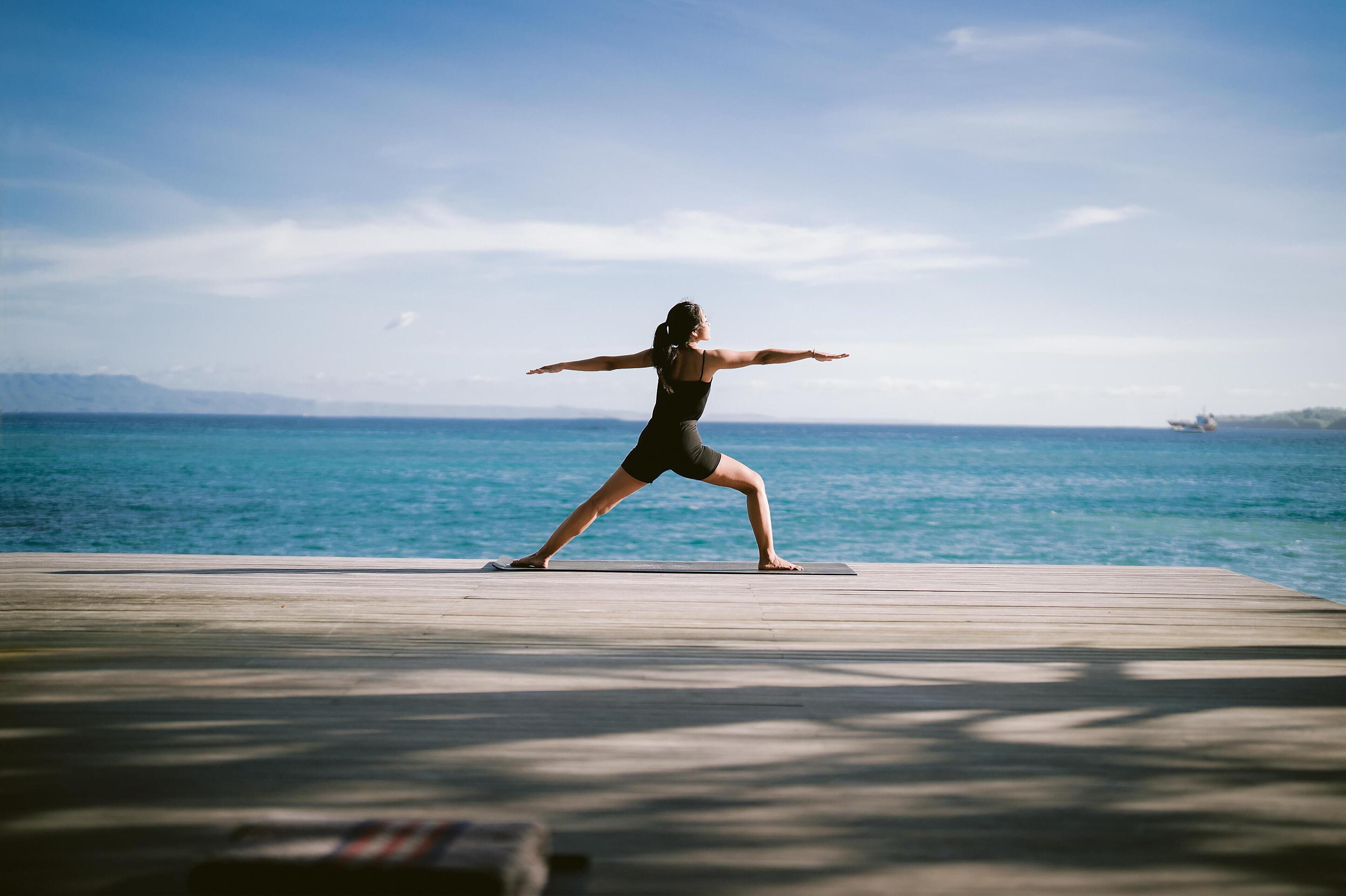 A person performing a yoga pose on a wooden deck by the sea.