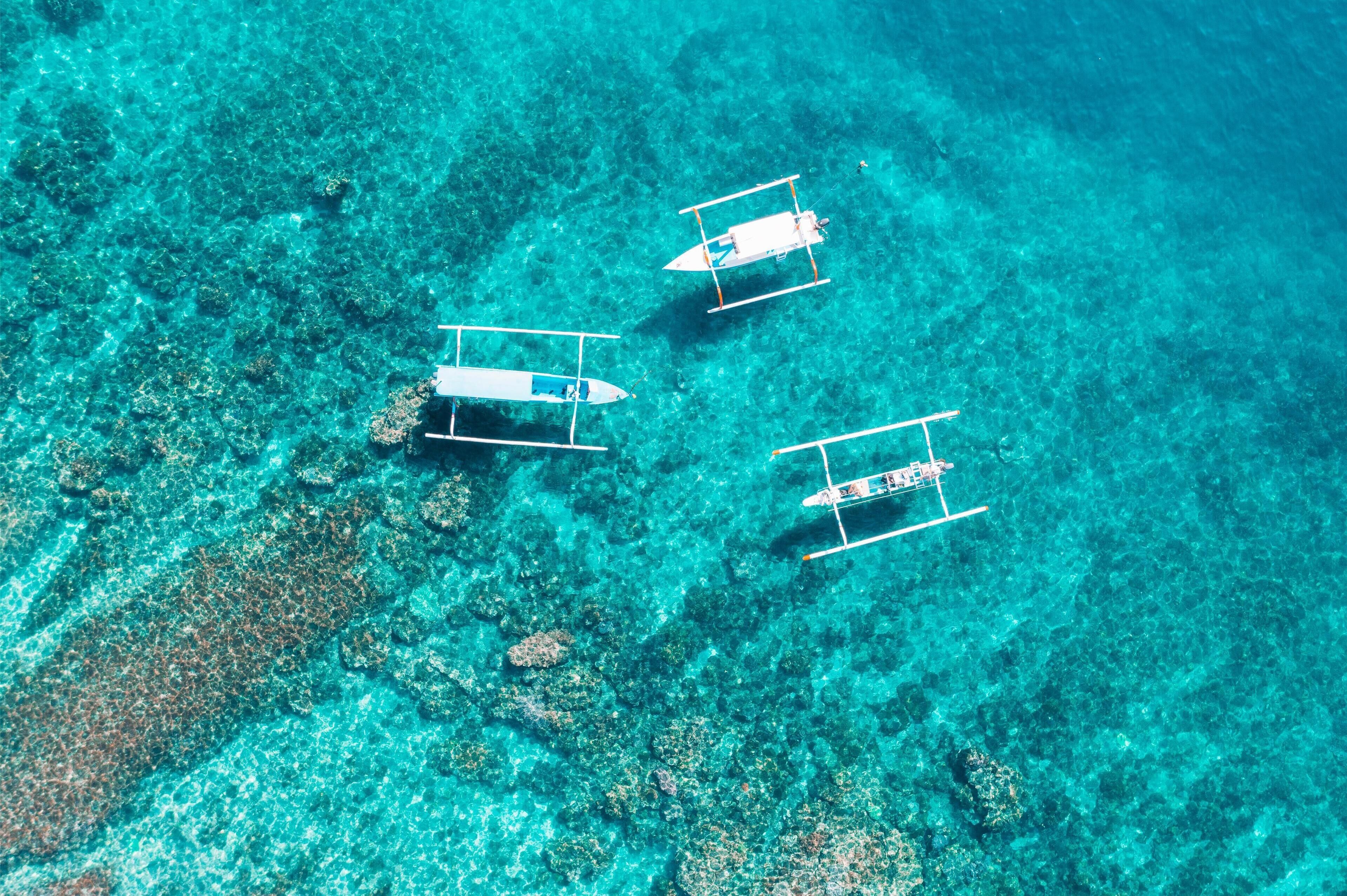 Three boats anchored in clear turquoise water with coral reefs visible beneath.