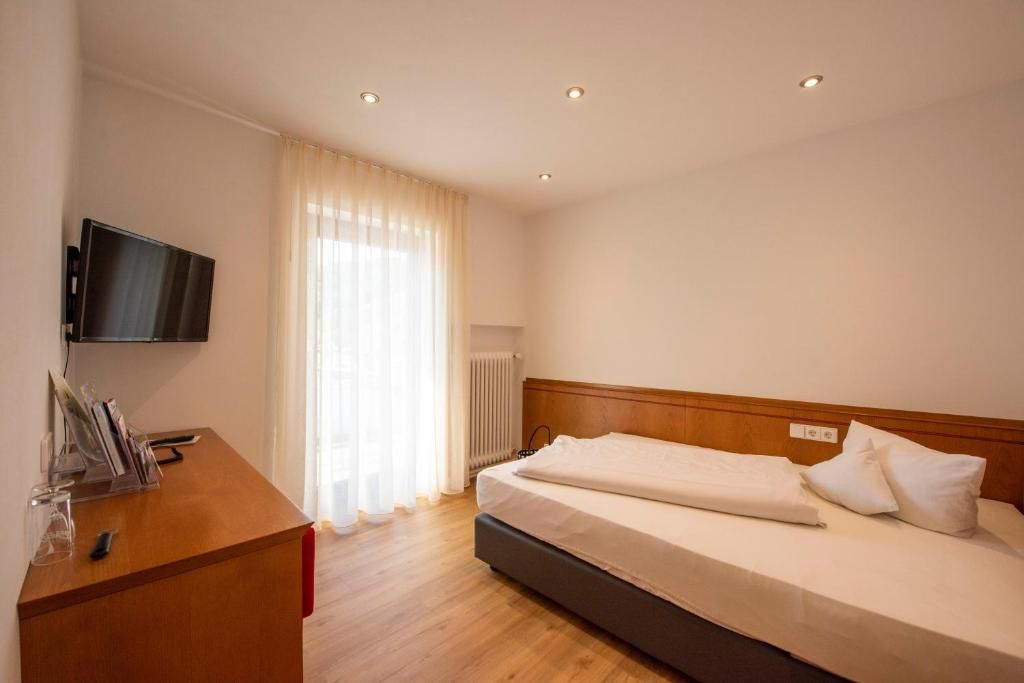 A hotel room with a bed, a desk with a flat-screen TV, and a window with curtains.
