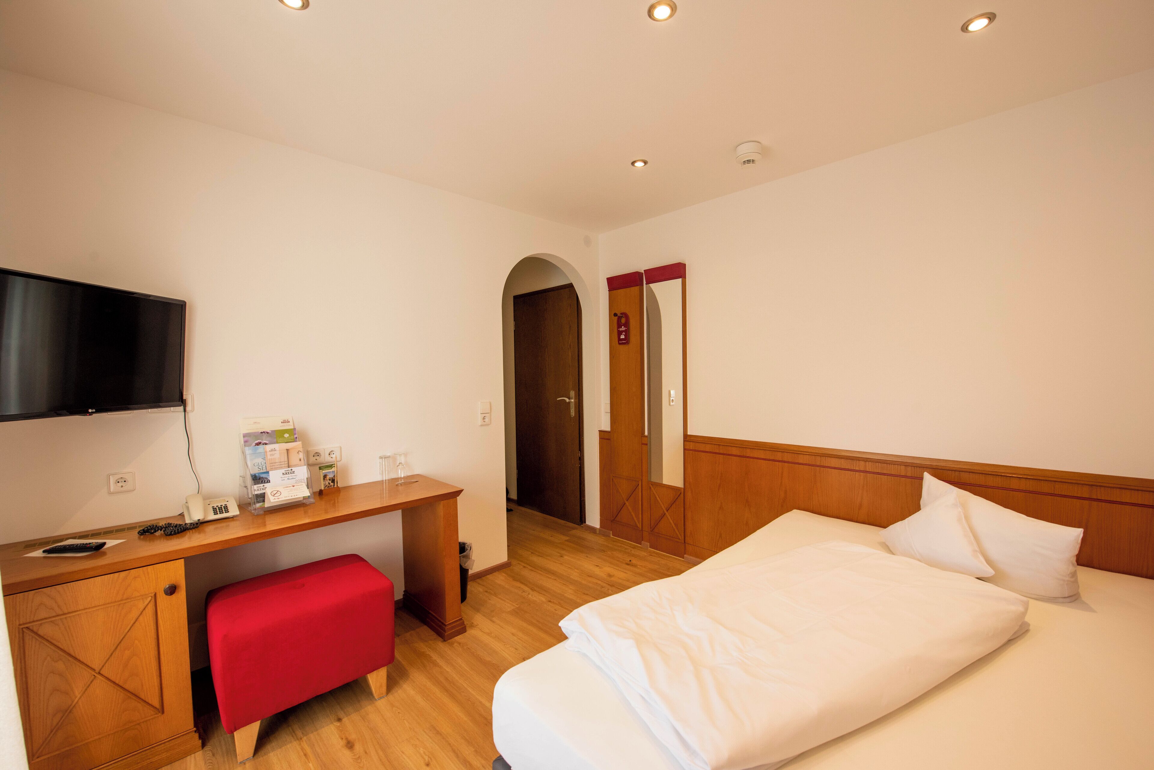 Ein Hotelzimmer mit einem Bett, einem Schreibtisch, einer roten Bank, einem Fernseher und einer Tür zu einem anderen Raum.