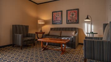 Quarto de hotel com uma poltrona listrada, um sofá, uma mesa de centro de madeira e duas fotos emolduradas na parede.