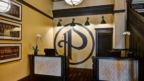 A reception area with a large circular logo, framed signs for train schedules, and a staircase. - Tapestry by Hilton The Peery Salt Lake City Downtown, UT (Salt Lake City)