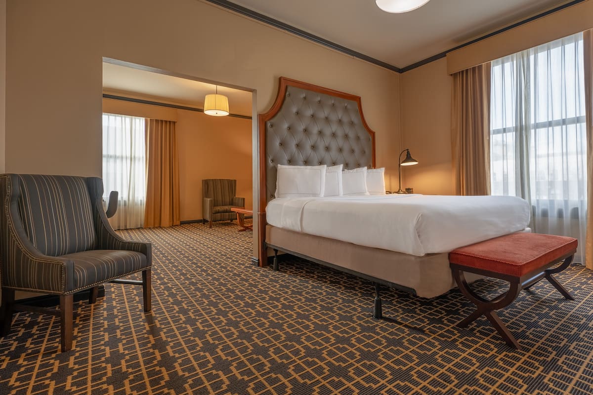 Une chambre d’hôtel avec un grand lit, une chaise, un banc et une moquette à motifs.