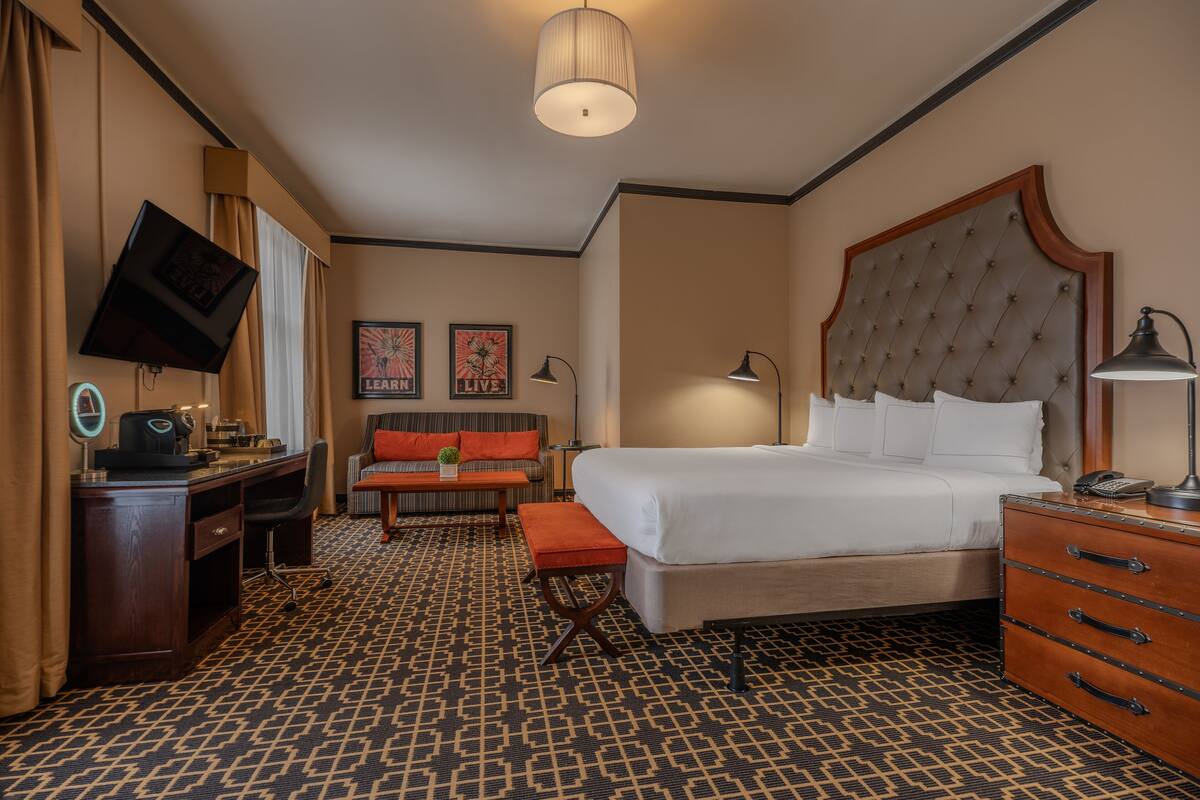 Une chambre d’hôtel avec un grand lit, un bureau avec un ordinateur, une chaise, un canapé et un téléviseur fixé au mur.