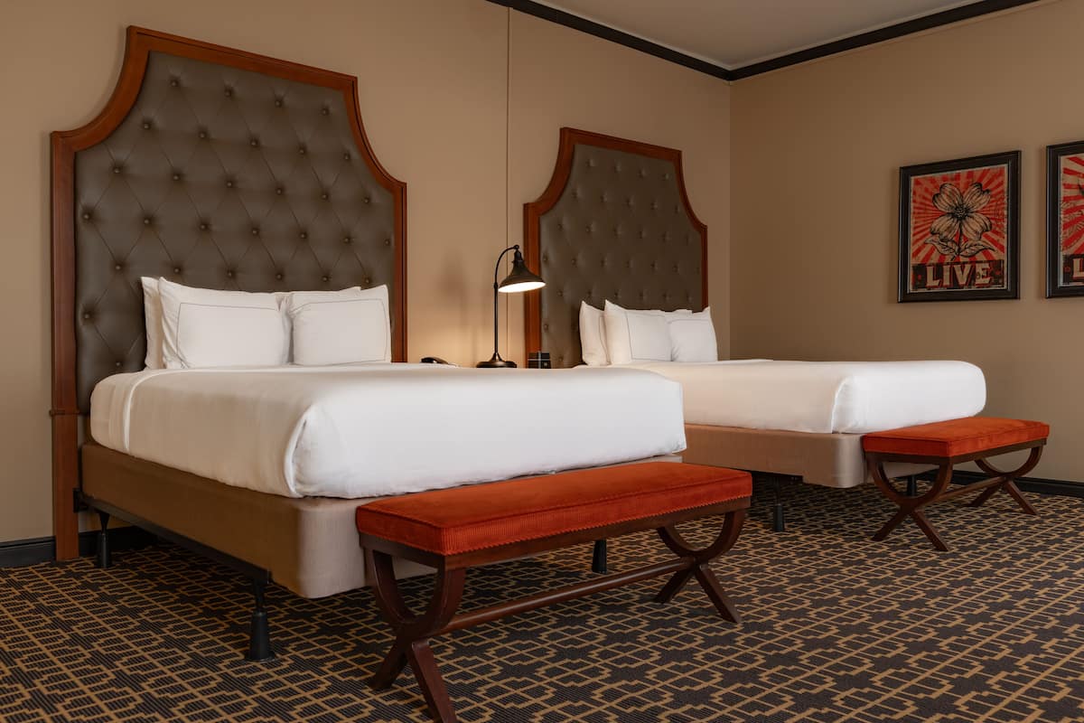 Une chambre d’hôtel avec deux lits, un banc, une lampe et deux tableaux encadrés au mur.