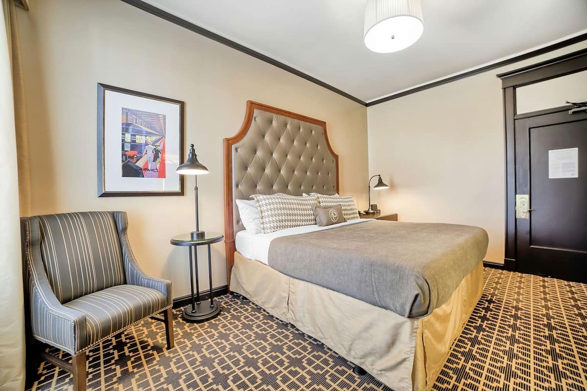 Une chambre d’hôtel avec un lit, une chaise, une lampe sur pied et une porte.