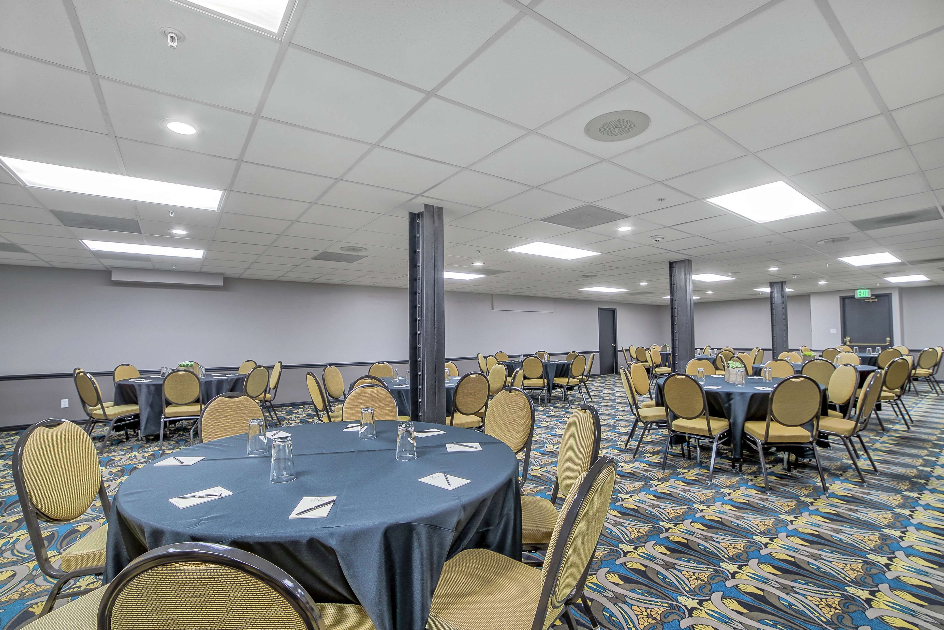 Un salón de conferencias con mesas redondas, sillas y piso alfombrado.