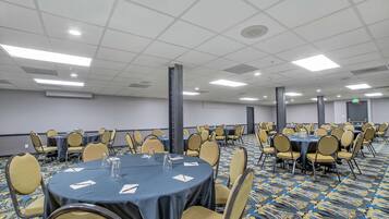 Un salón de conferencias con mesas redondas, sillas y piso alfombrado.
